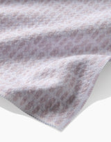 A close-up of the Dot Dot Dot Blushed Bergamot tea towel by Geometry, featuring soft, ultra-absorbent fabric and a subtle light purple and white geometric pattern along the edge’s gentle folds.