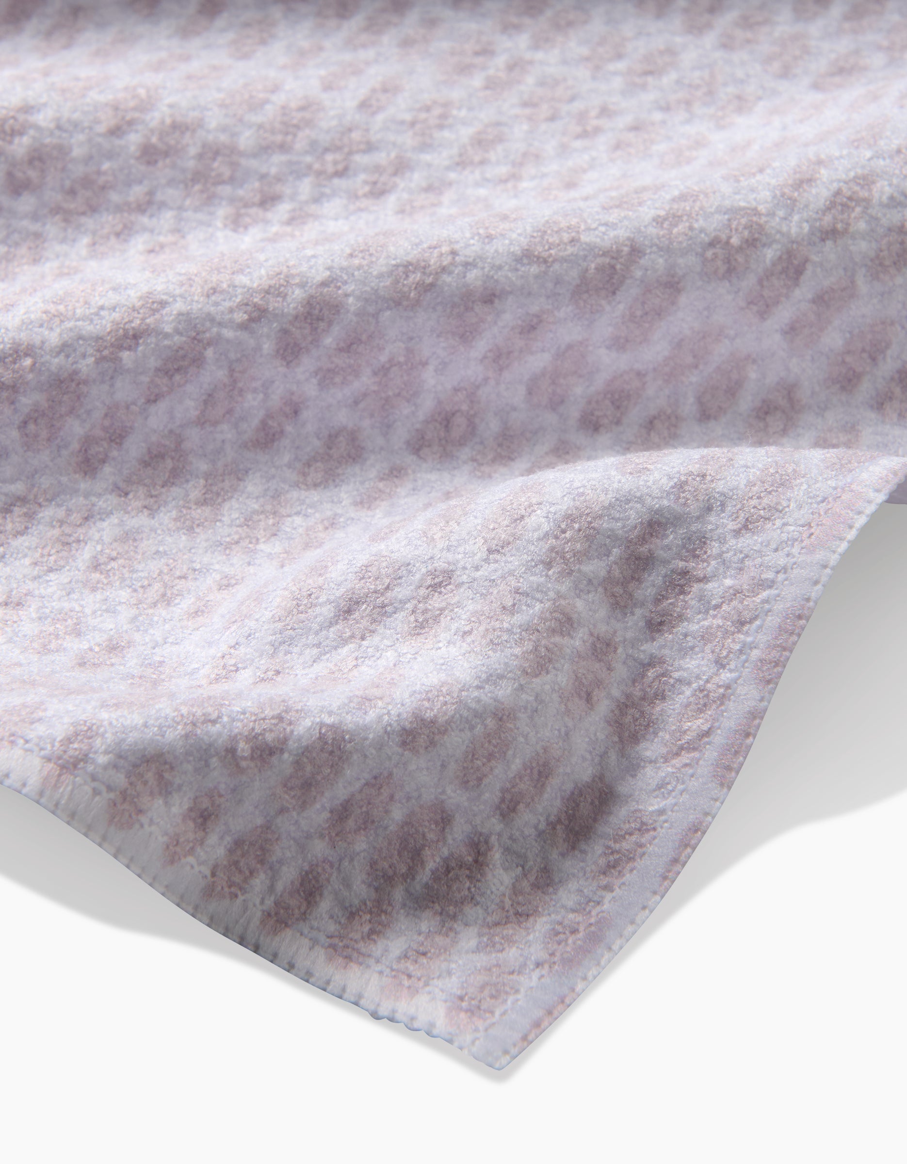 A close-up of the Dot Dot Dot Blushed Bergamot tea towel by Geometry, featuring soft, ultra-absorbent fabric and a subtle light purple and white geometric pattern along the edge’s gentle folds.