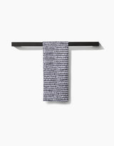 The Geometry Dot Dot Dot Fresh Linen, a white ultra-absorbent towel with black irregular dots, hangs neatly on a minimalist black towel bar against a plain white background.