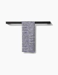 The Geometry Dot Dot Dot Fresh Linen, a white ultra-absorbent towel with black irregular dots, hangs neatly on a minimalist black towel bar against a plain white background.