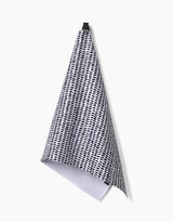 The Geometry Dot Dot Dot Fresh Linen ultra-absorbent tea towel, featuring a black and white dotted grid pattern, hangs from a black hook against a plain white background.