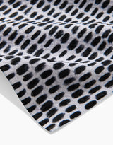 A close-up of Geometry’s Dot Dot Dot Fresh Linen tea towel shows its black abstract oval dot pattern on white, emphasizing the ultra-absorbent fabric’s texture and folds.