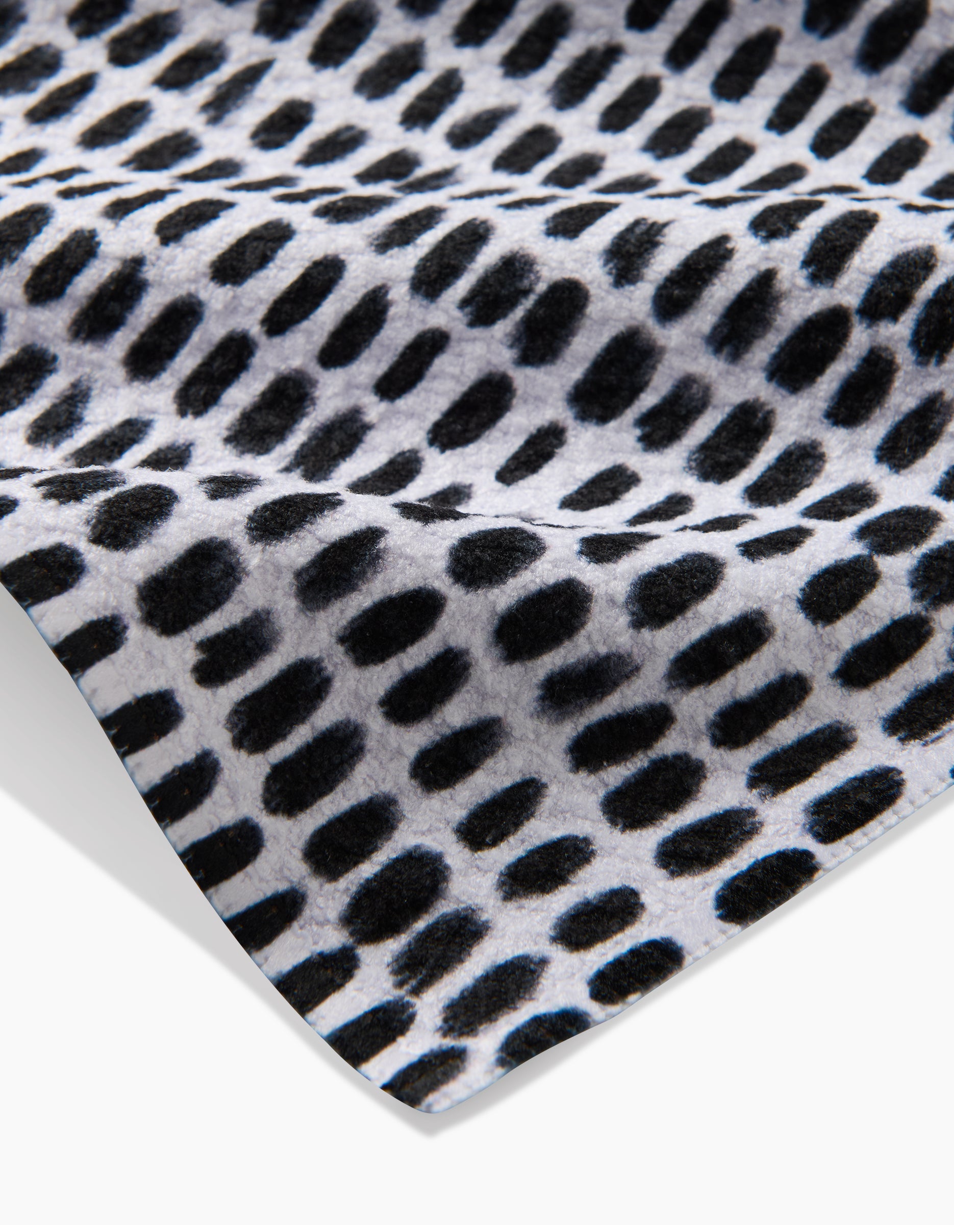 A close-up of Geometry’s Dot Dot Dot Fresh Linen tea towel shows its black abstract oval dot pattern on white, emphasizing the ultra-absorbent fabric’s texture and folds.