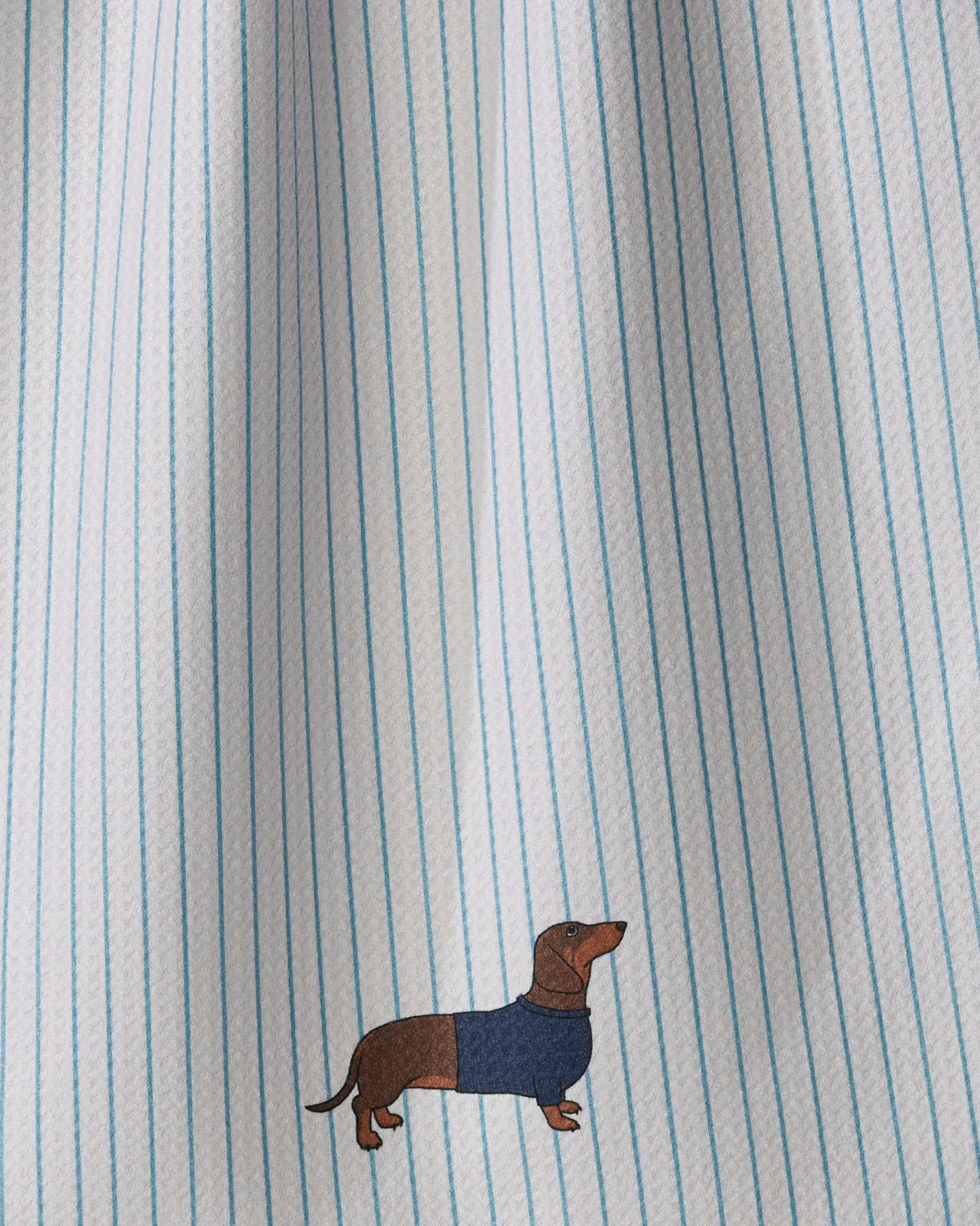 The Geometry Doxie Stripe kitchen tea towel is white with thin blue vertical stripes and features a small embroidered brown dachshund wearing a blue sweater near the bottom.