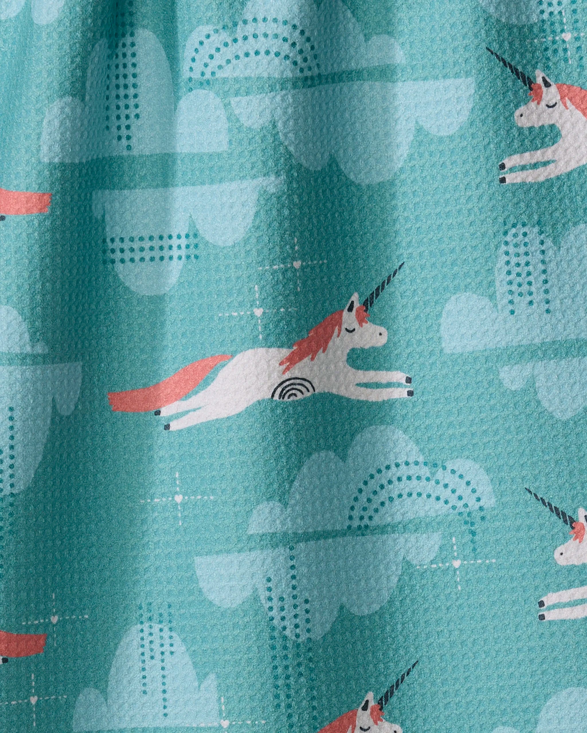 The Dream the Best tea towel by Jessica Swift features whimsical white unicorns with pink manes, black horns, and dotted accents leaping among blue clouds on aqua fabric, crafted from ultra-absorbent recycled materials.