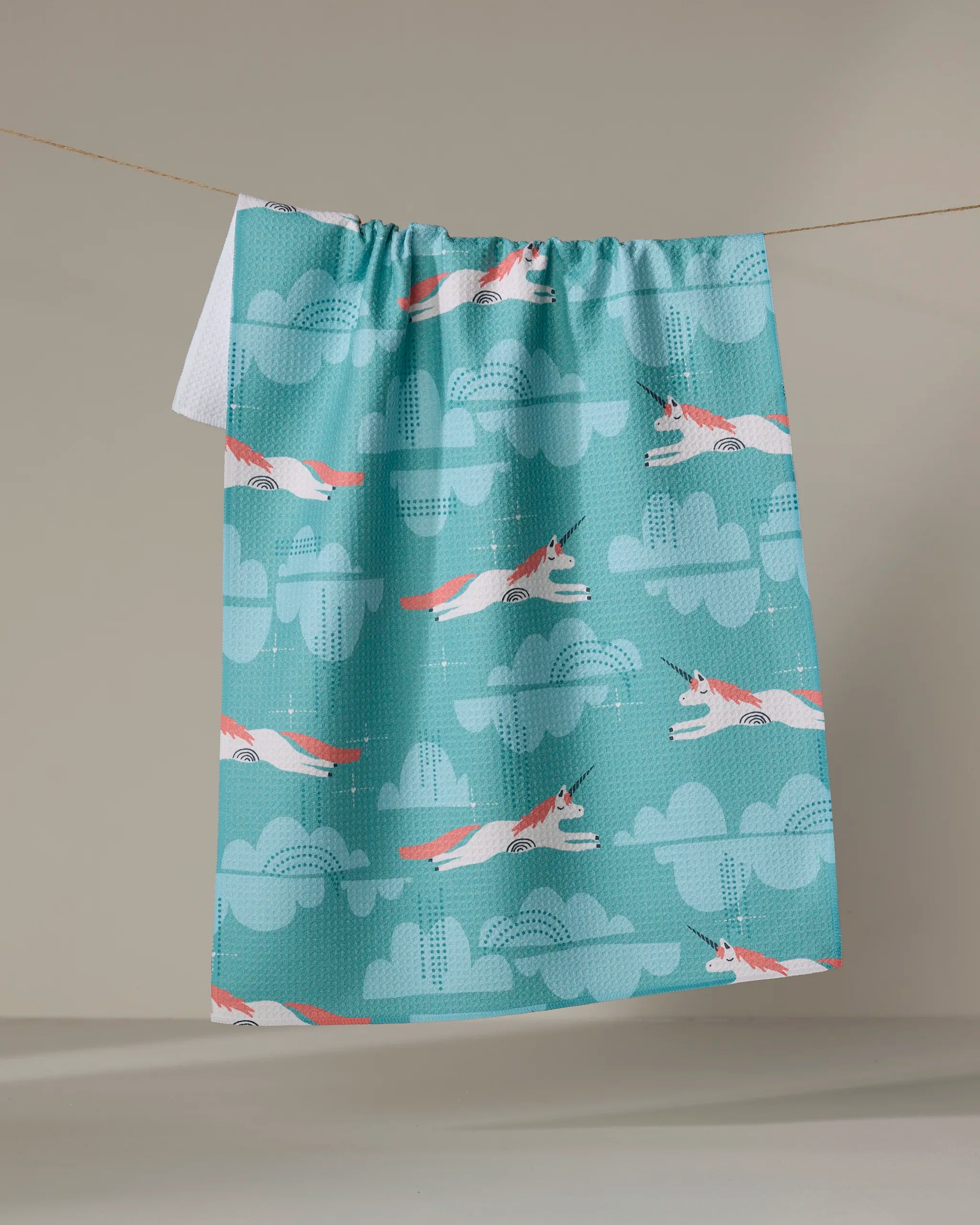 The "Dream the Best" tea towel by Jessica Swift, made from recycled materials and adorned with a playful fox and cloud design, hangs on a line against a neutral background.