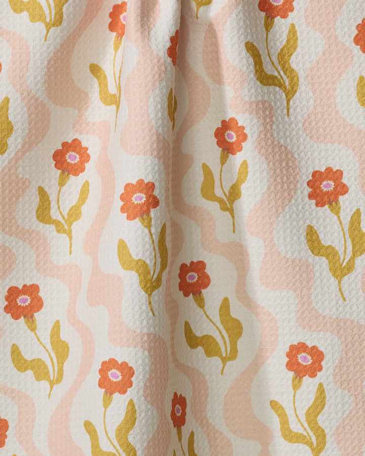 The Dreamy Path tea towel by Gerdadzy features a wavy pink and cream background with red flowers and yellow stems, crafted from recycled materials for an eco-friendly touch.