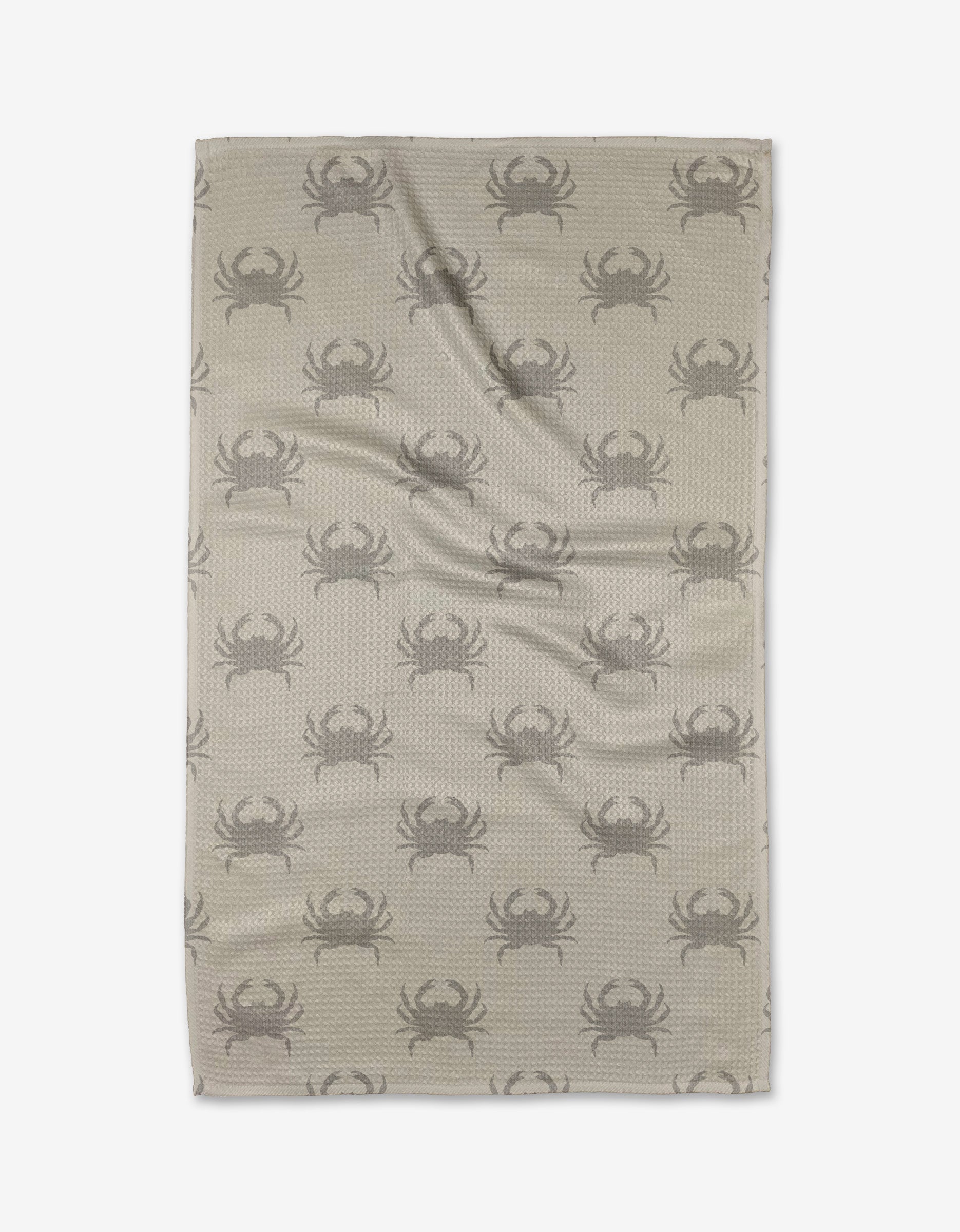 The Dungeness Days tea towel by Jenny Keller features a beige backdrop with a repeating dark gray crab pattern. Made from quick-drying, recycled materials for eco-friendly convenience. Shown flat with slight wrinkles on a white background.
