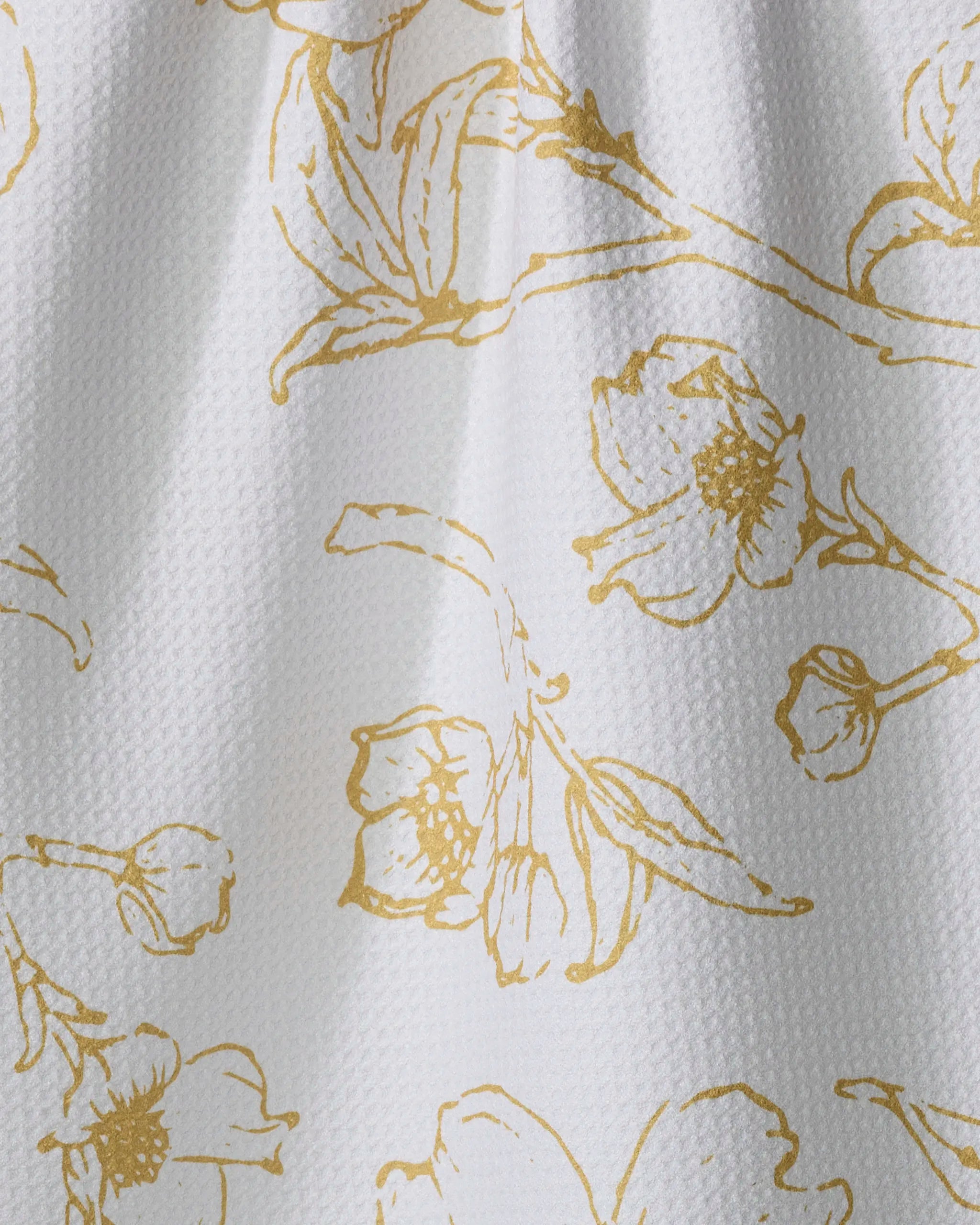 Close-up of the Ashley Celena "Early Blossoms" tea towel, showcasing gold sketch-style floral and leaf patterns on absorbent white fabric. Its delicate design and gentle folds add an elegant touch to any kitchen.
