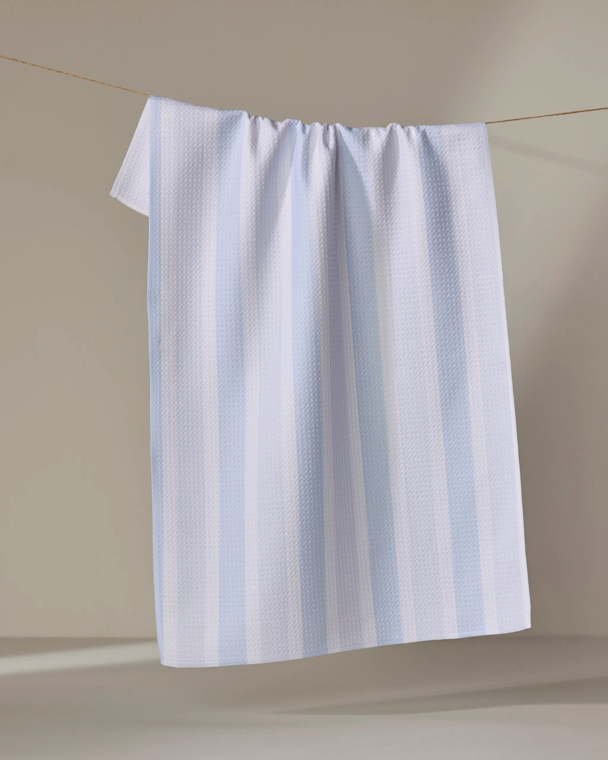 The Buy Guide’s Earn Your Stripes - Light Blue tea towel, made from recycled materials, features absorbent fabric, a light blue and white stripe design, and a subtle textured pattern for stylish function in any kitchen.