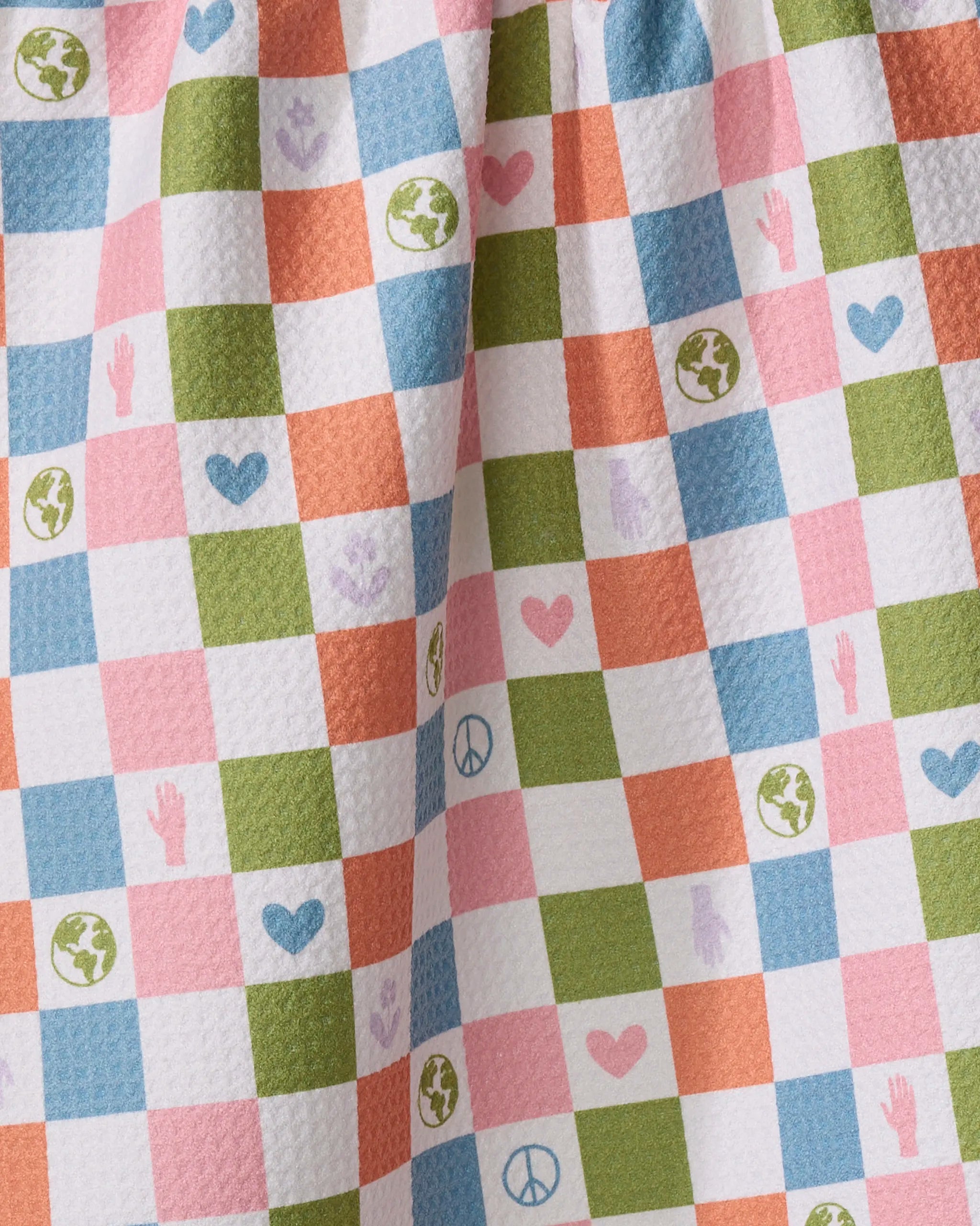 The Kayla Ann Earth Day Checkers tea towel features blue, green, pink, and orange squares with hearts, globes, peace signs, and handprints. Made from recycled materials, it’s ultra-absorbent with a slightly gathered look.