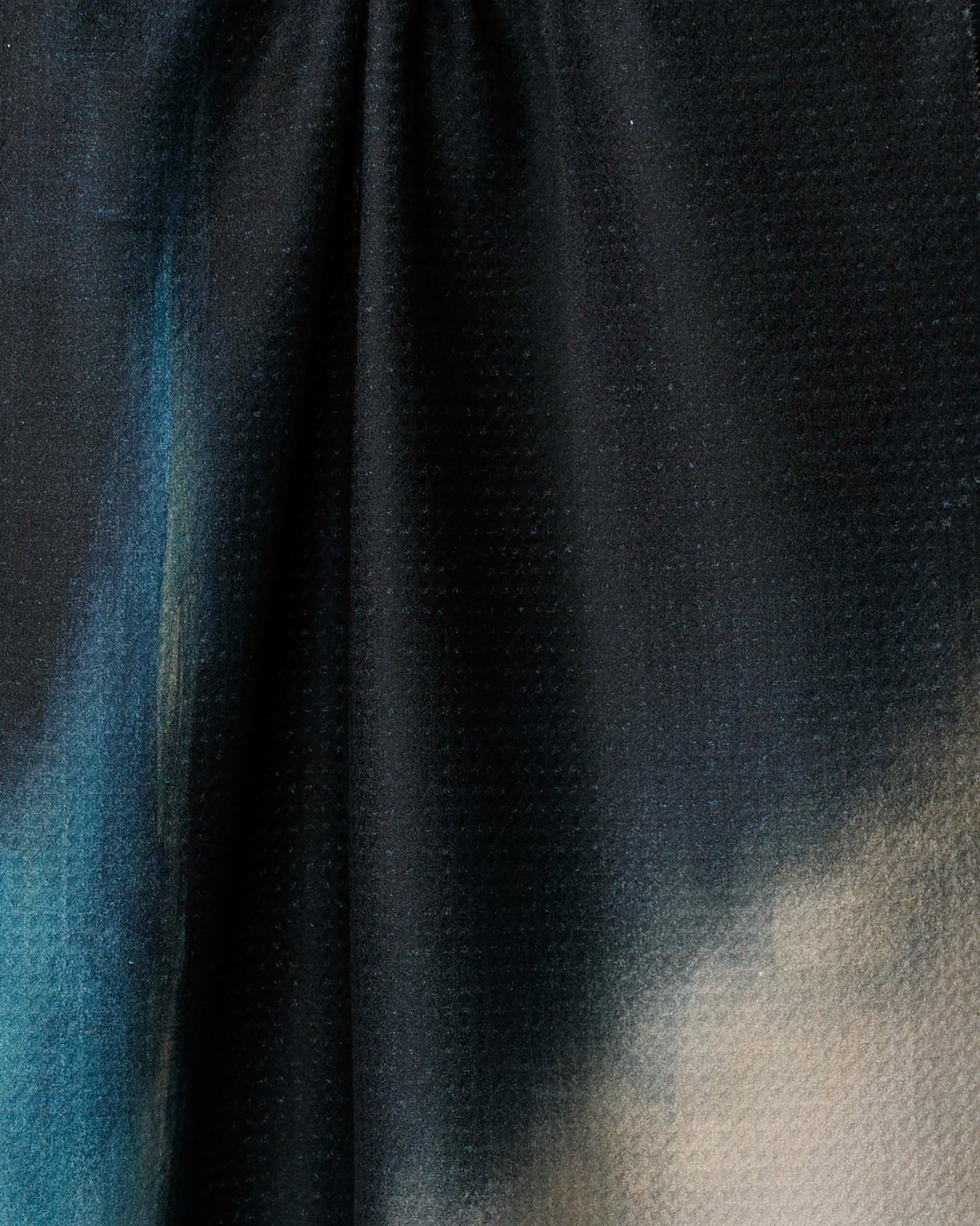 A close-up of Earth Erupted by Jennifer Janesko: this kitchen towel showcases dark, subtly textured fabric with blue and beige gradients. Made from recycled materials, it’s gently gathered at the top, forming soft folds and shadows.