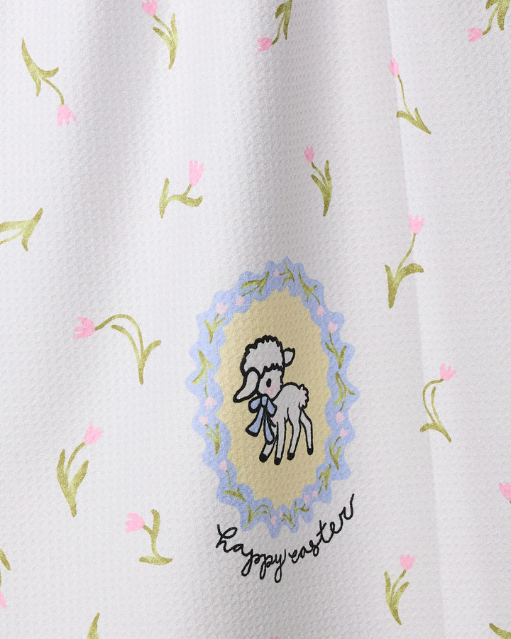 The Easter Little Lamb tea towel by Geometry features a white textured design with light green and pink floral sprigs, an illustrated lamb within a pastel scalloped border, “Happy Easter” text, and is crafted from recycled materials for eco-friendliness.