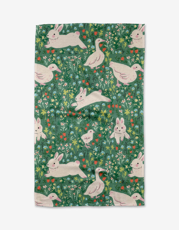 The Easter Meadow kitchen towel by Janna Sue Design is an eco-friendly green towel decorated with white rabbits, ducks, and wildflowers for a whimsical, nature-inspired look.