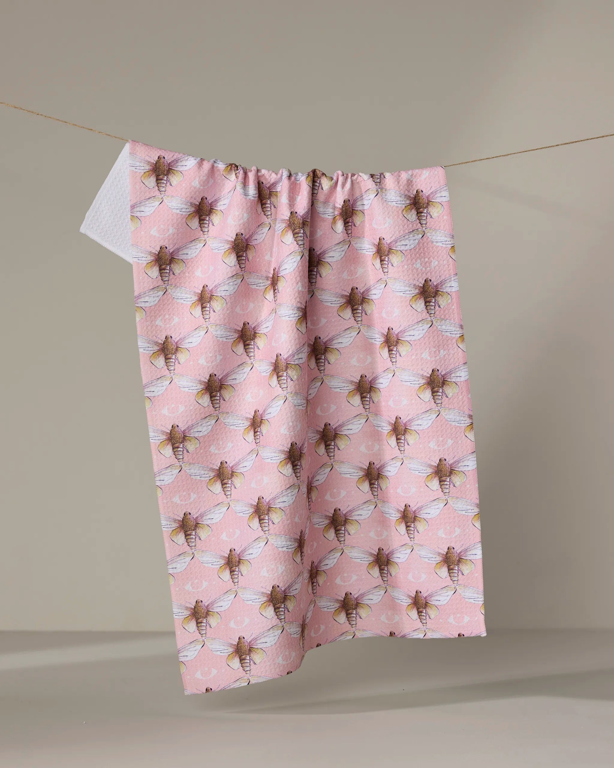 Echo, a quick-drying pink tea towel by Maayan Alper-Swan, displays a repeating bee pattern and hangs on a clothesline against a neutral background.