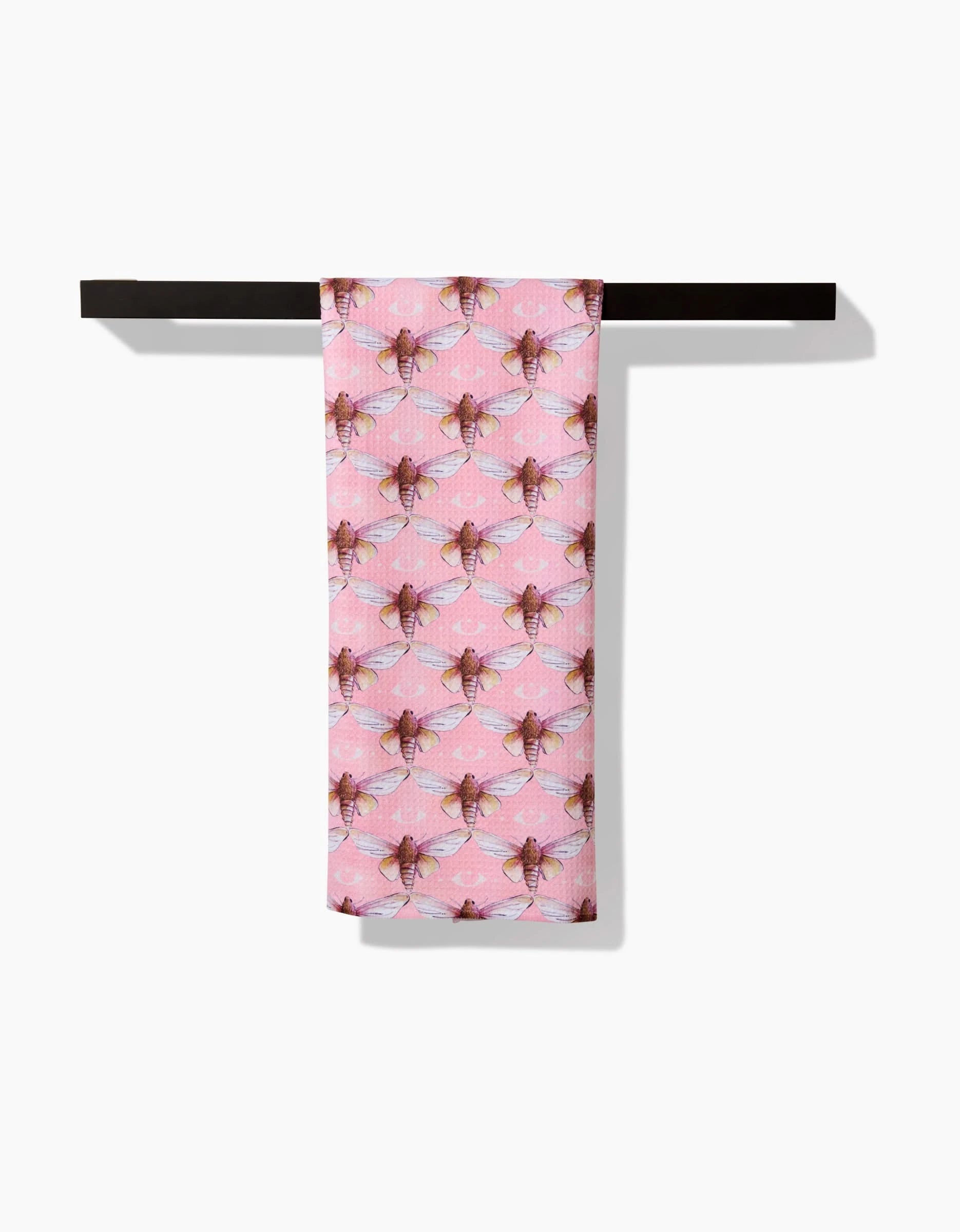 The Echo towel by Maayan Alper-Swan, featuring a repeating bee pattern and made from ultra-absorbent Geoweave fabric in pink, hangs neatly over a simple black bar against a white background.