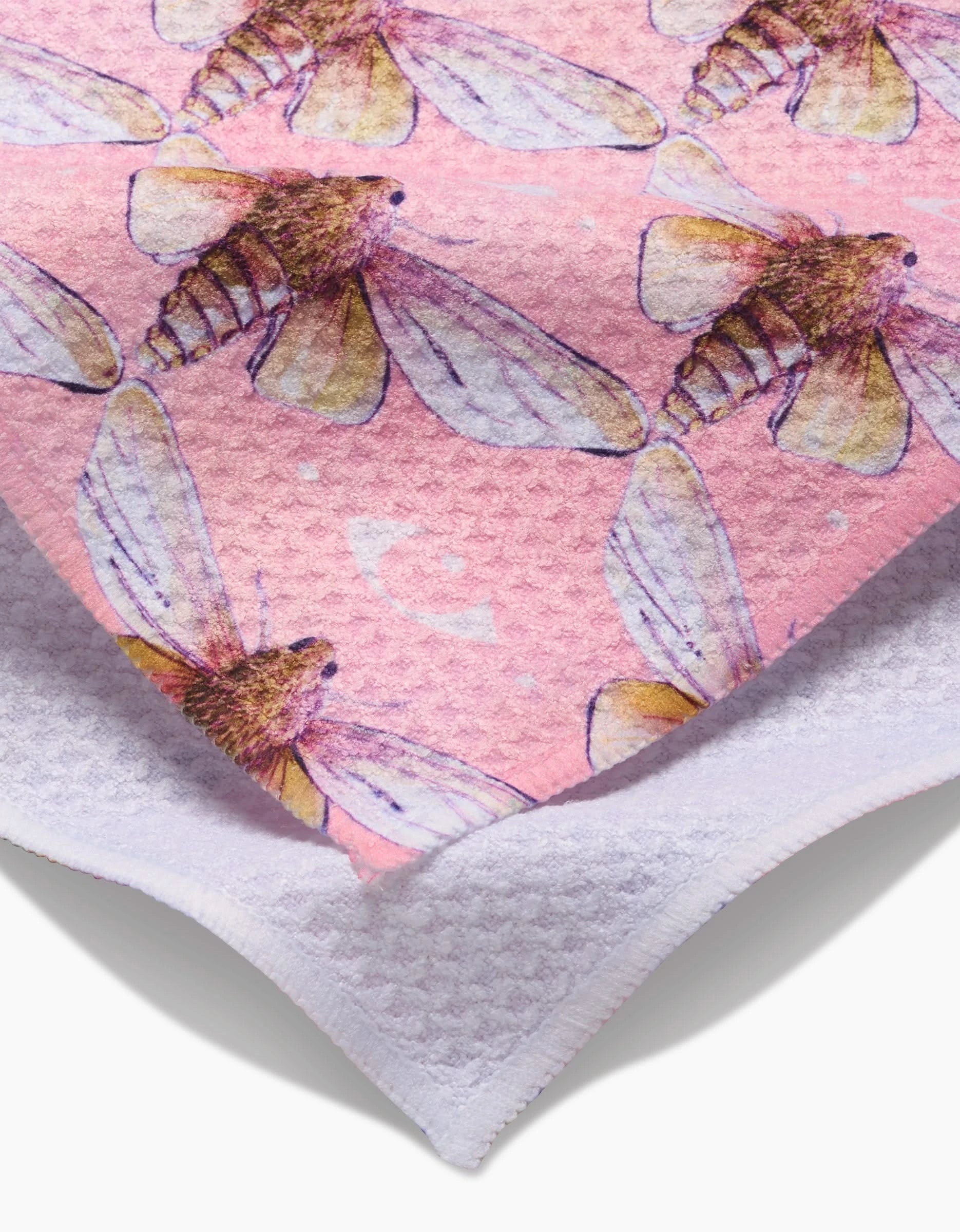 A close-up of Maayan Alper-Swans Echo pink towel, adorned with watercolor-style moths with translucent wings and brown bodies, layered atop an ultra-absorbent white textured towel.