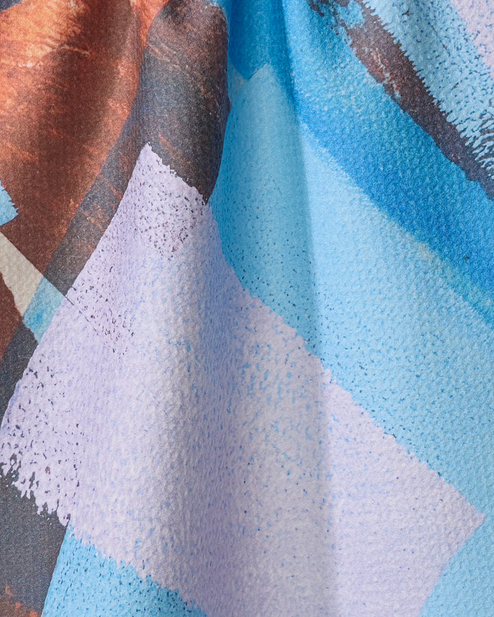 Echoes of Color by Skye Walker is a kitchen tea towel made from recycled materials, featuring a textured pattern in blue, purple, brown, and white with overlapping geometric shapes and brushstroke-inspired details.