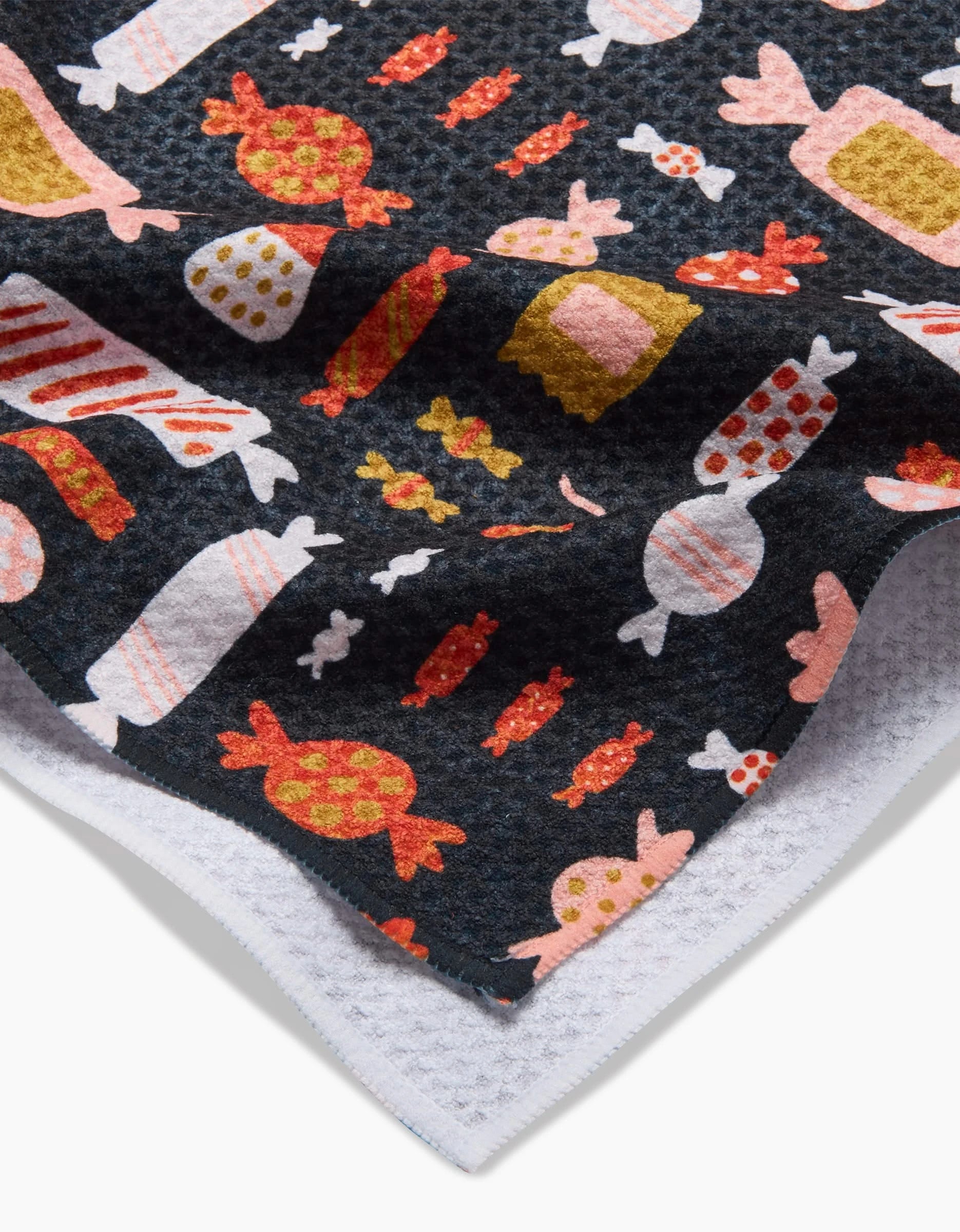 A close-up of the Edwina Tea Towel by Amy MacCready, crafted from recycled materials with colorful candy illustrations in orange, pink, red, and yellow, finished with a white waffle-patterned edge.