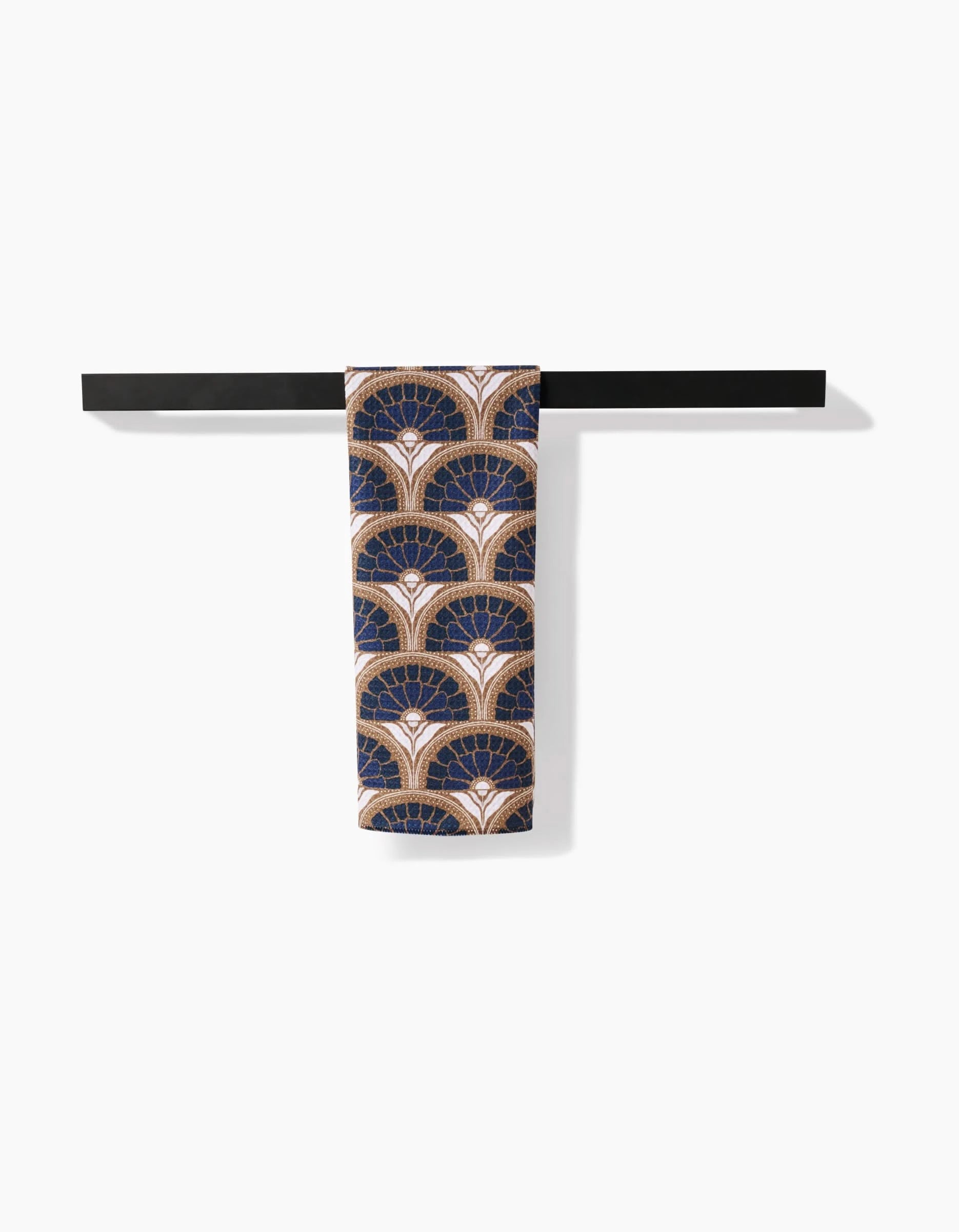 The Eliza tea towel by Amy MacCready, featuring a navy blue and gold art deco fan pattern and crafted from recycled materials, is draped over a sleek black horizontal towel bar against a white background.