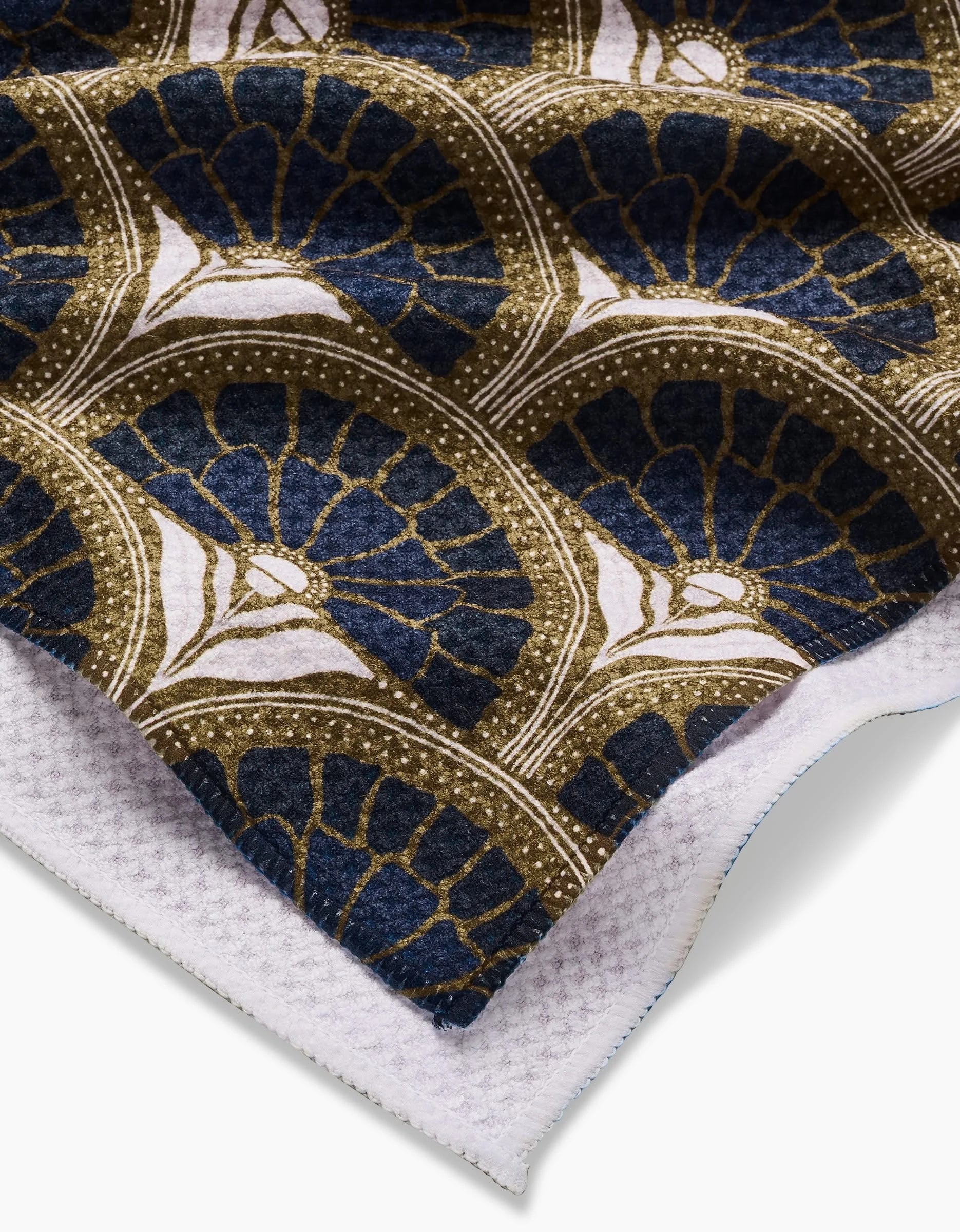 A close-up of the Eliza tea towel by Amy MacCready, showcasing a dark blue, gold, and white geometric fan pattern. The textured underside is ultra-absorbent and crafted from recycled materials.