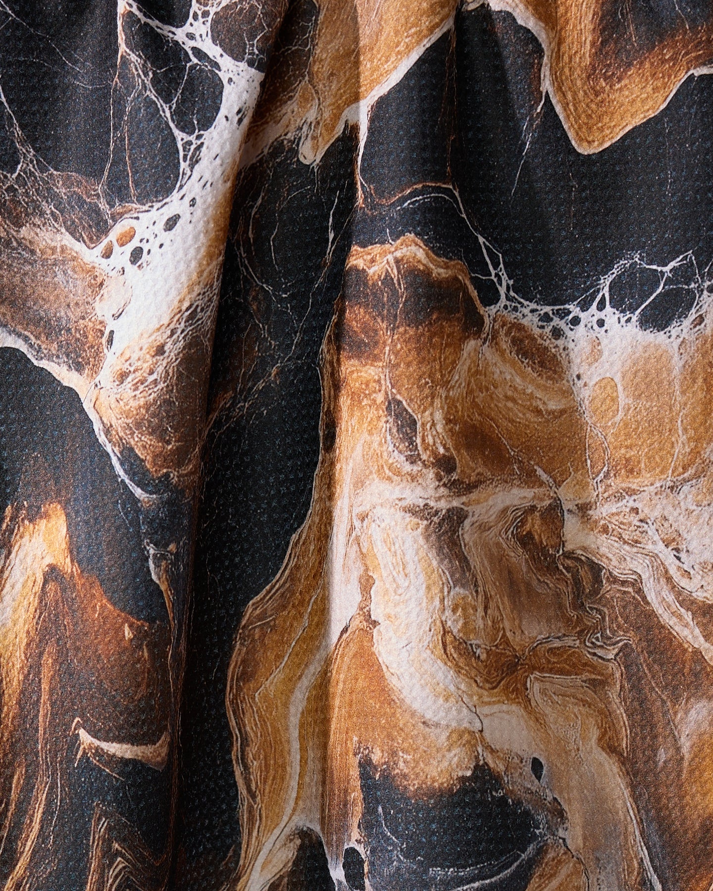 A close-up of Geometry’s Emperador tea towel showcases its absorbent material and marbled black, brown, and white pattern with swirling, stone-like textures and soft folds.