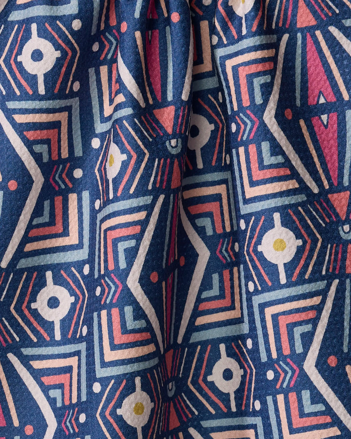 A close-up of Jessica Swift's Energetics towel, featuring an ultra-absorbent surface with a blue, pink, white, and yellow geometric pattern—lines, circles, arrows, and dots forming repeating shapes on gently wrinkled fabric.
