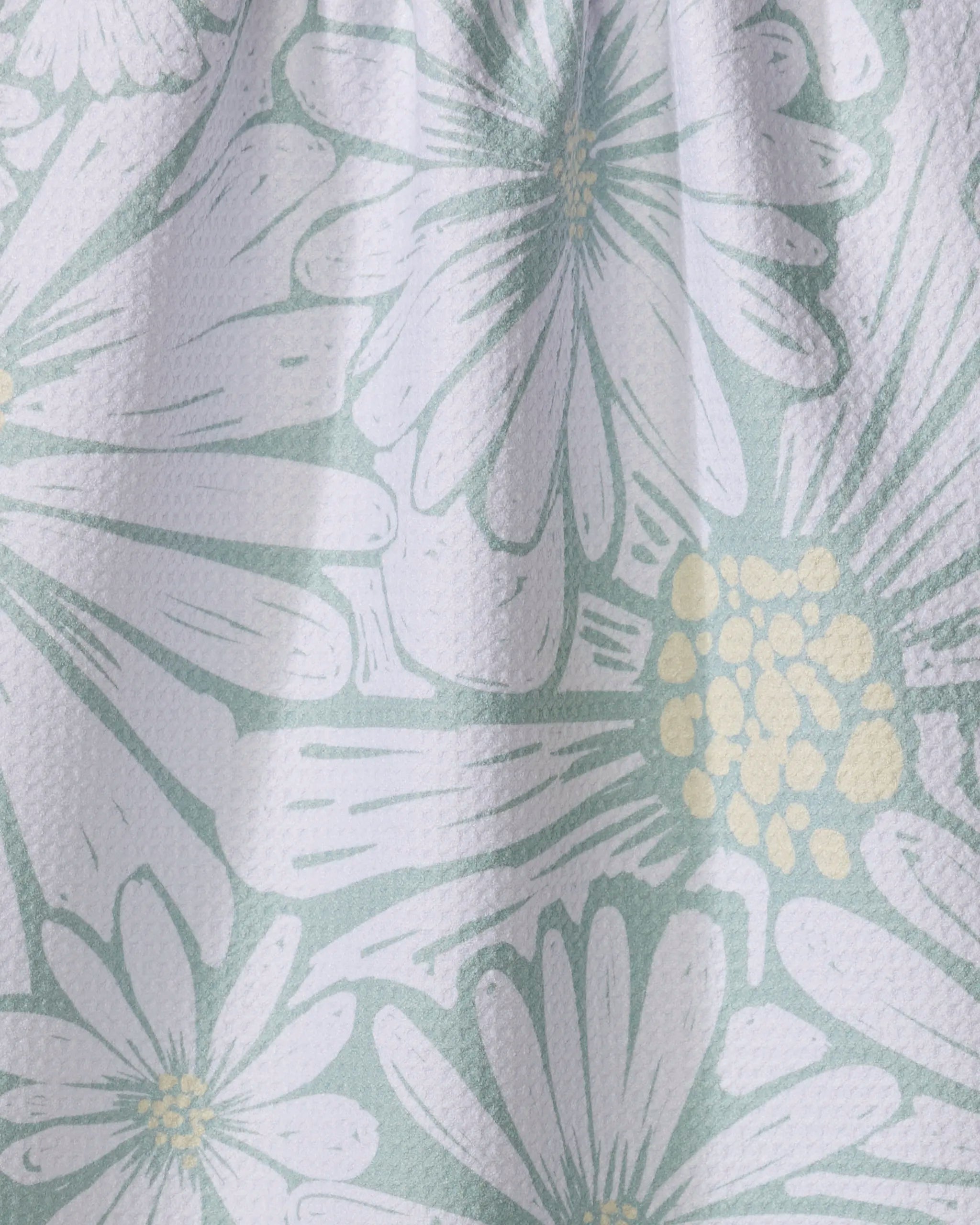Close-up of the "English Daisies" tea towel by Elisabeth Wing, showing a pastel floral pattern with large white flowers and yellow details on a light green background.
