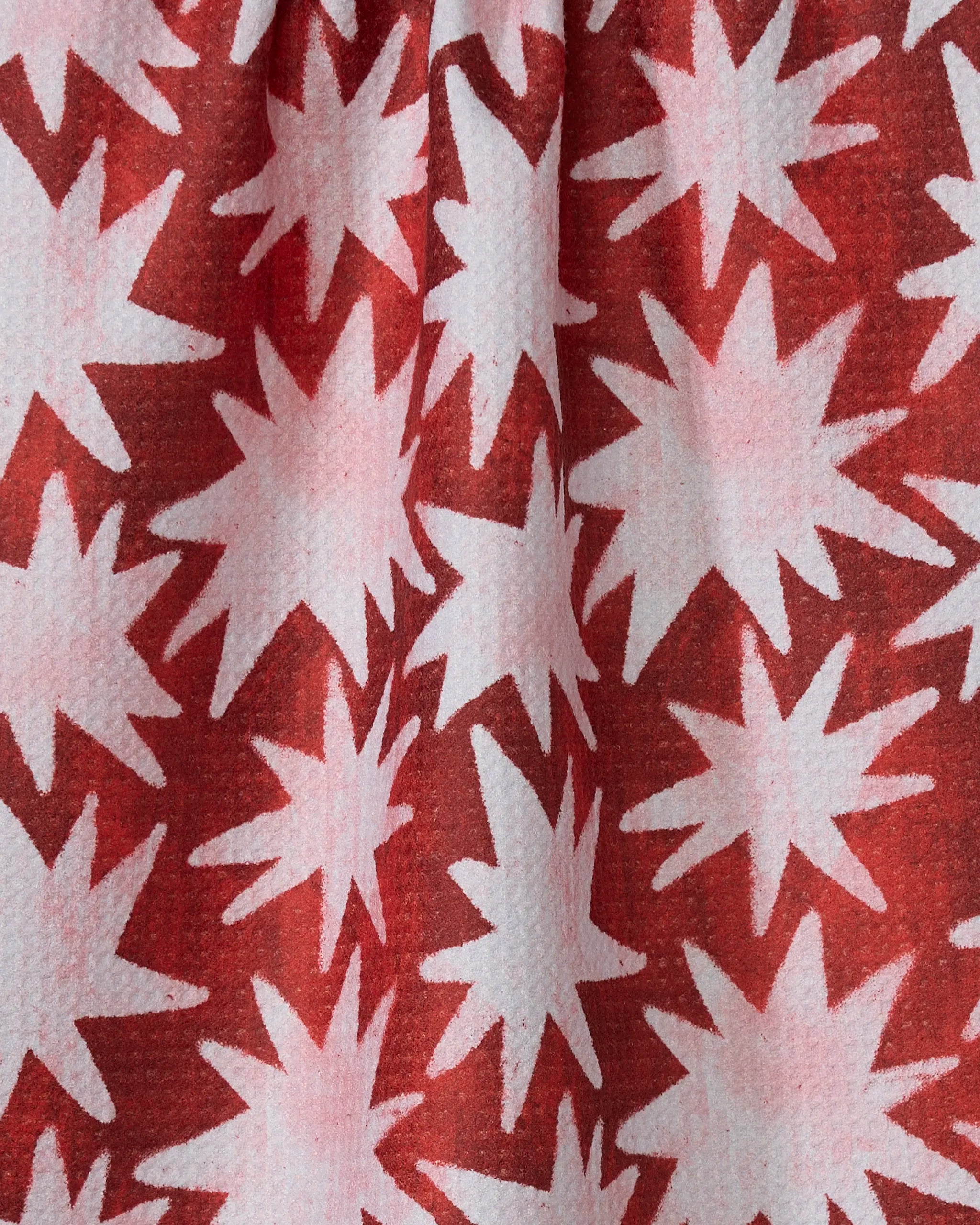The Estrellas tea towel by Geometry features a red background with white, starburst-like patterns and a textured finish. Made from recycled materials, this ultra-absorbent towel brings bold style to your kitchen décor.