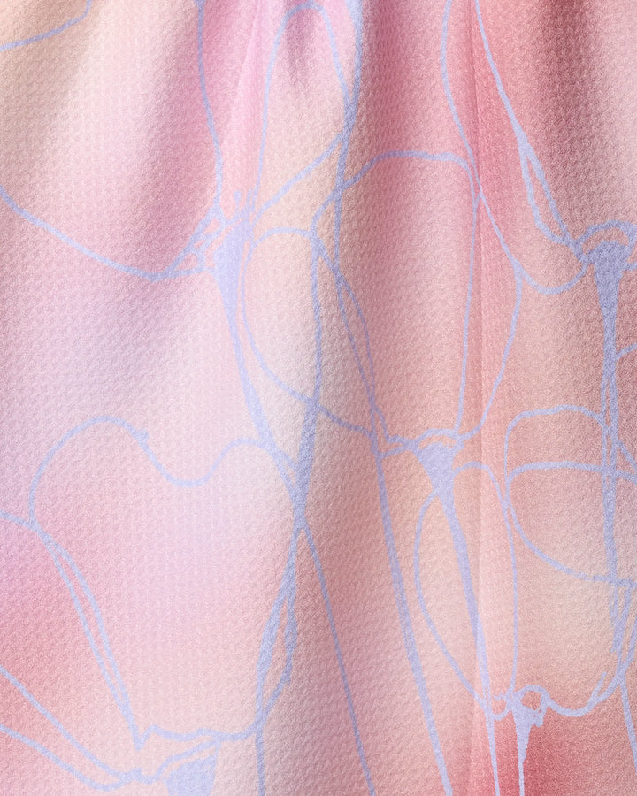 Close-up of Geometry’s Ethereal Bloom kitchen towel, made from recycled materials. Its textured, gently rippled surface displays a delicate pattern against a soft pink and peach gradient background with thin, light blue abstract lines.