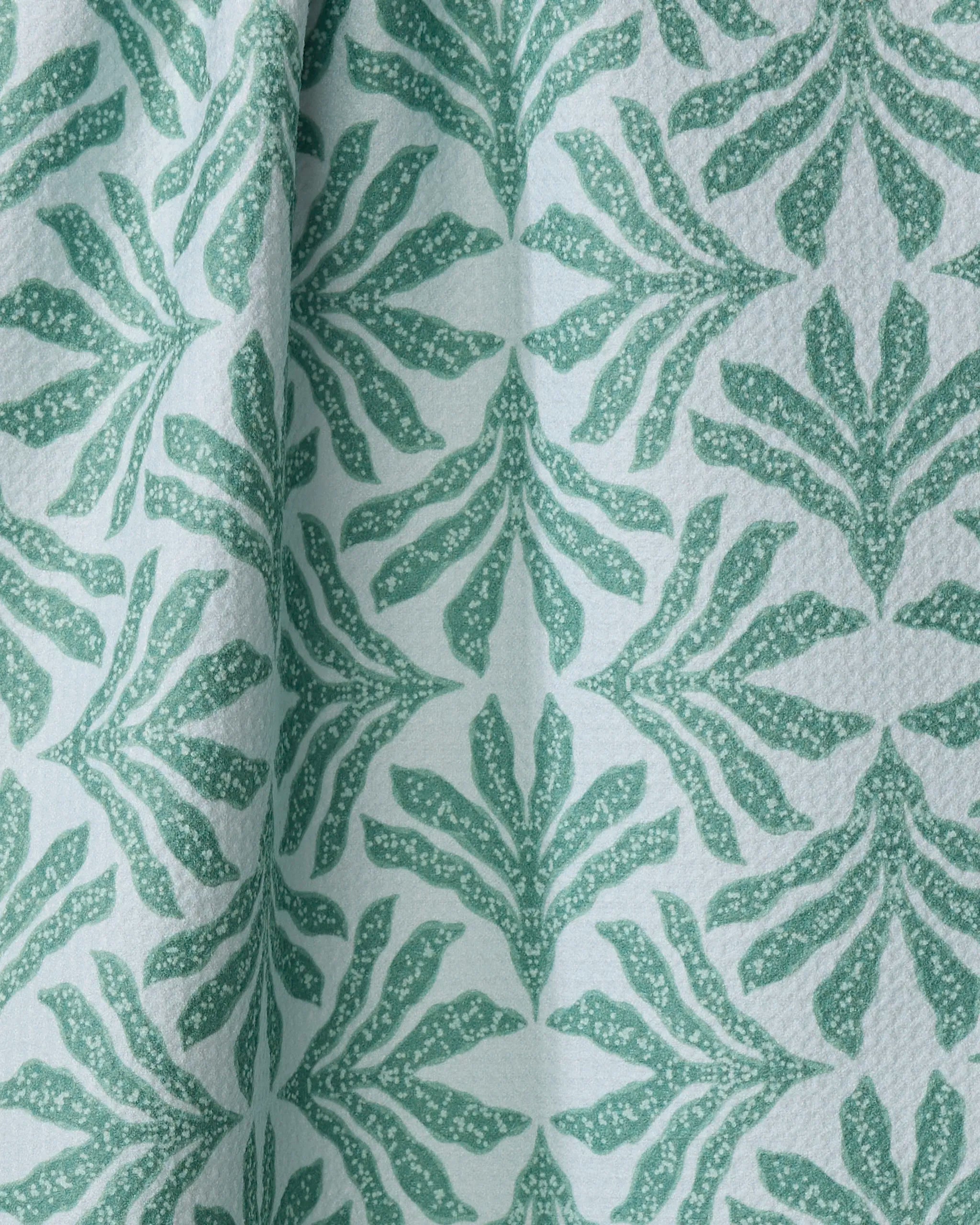 Close-up of the "Ethereal Seaweeds" tea towel by Jasmine Blooms Designs, crafted from recycled materials. Its soft, light blue fabric showcases a repeating pattern of green leafy seaweed shapes and graceful vertical folds.