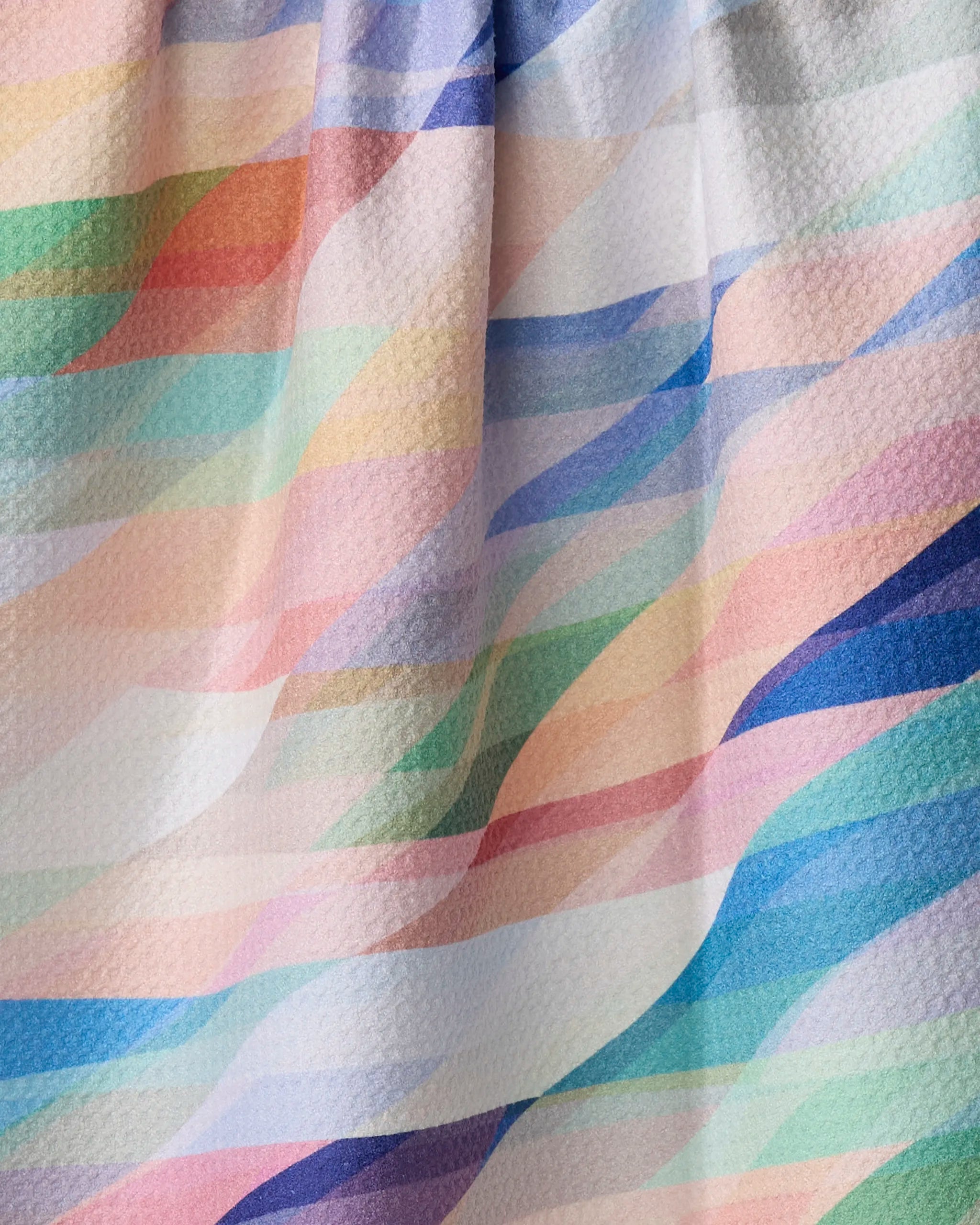 The Rachel Parker Eventide tea towel features a wavy, multicolored pastel design in pink, blue, green, yellow, and peach diagonals. Made from recycled materials with a textured finish.