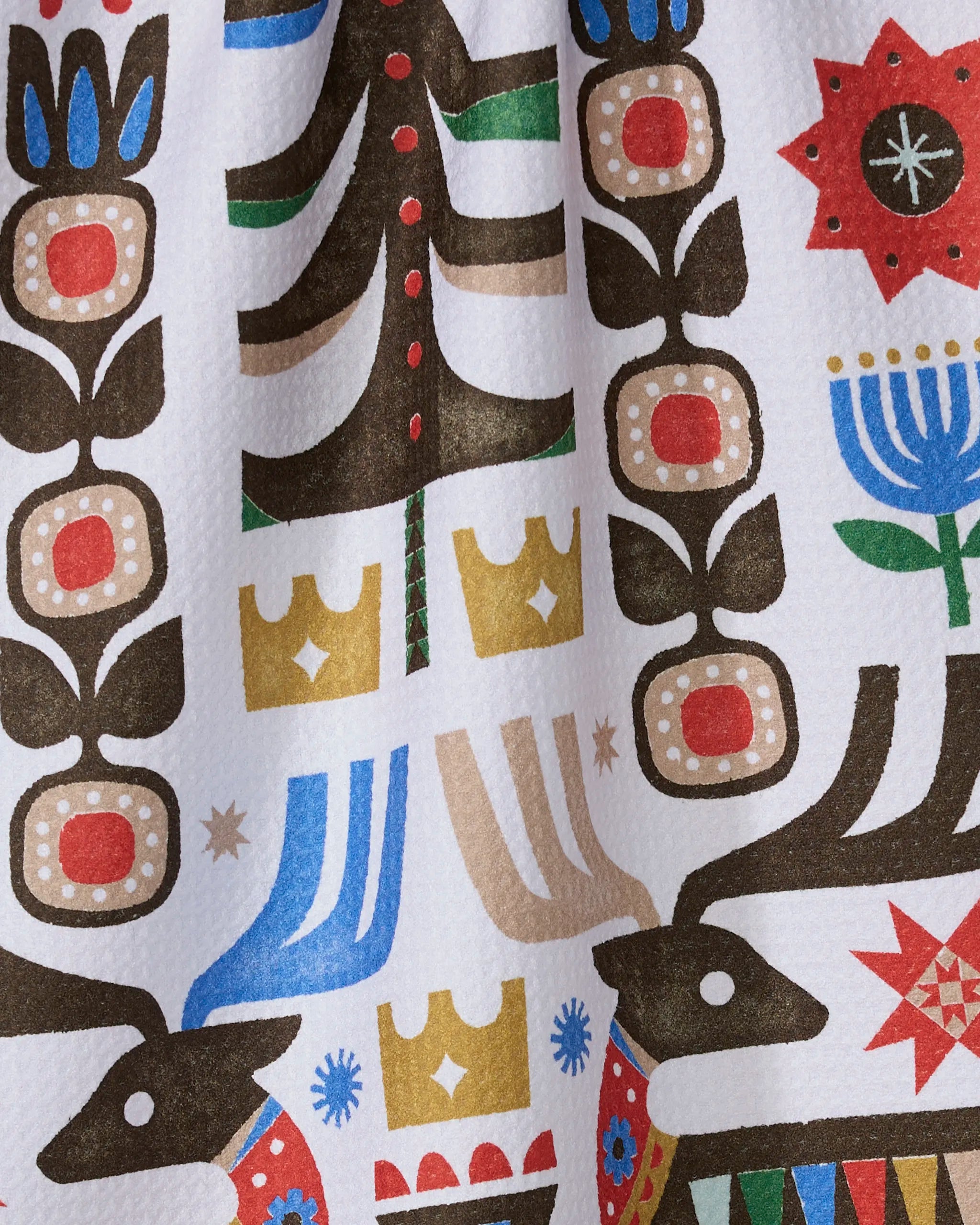 The Everfolk kitchen towel by Geometry features a vibrant folk art pattern with reindeer, flowers, trees, crowns, and geometric shapes in bold colors on white—eco-friendly and perfect for adding charm to your kitchen.