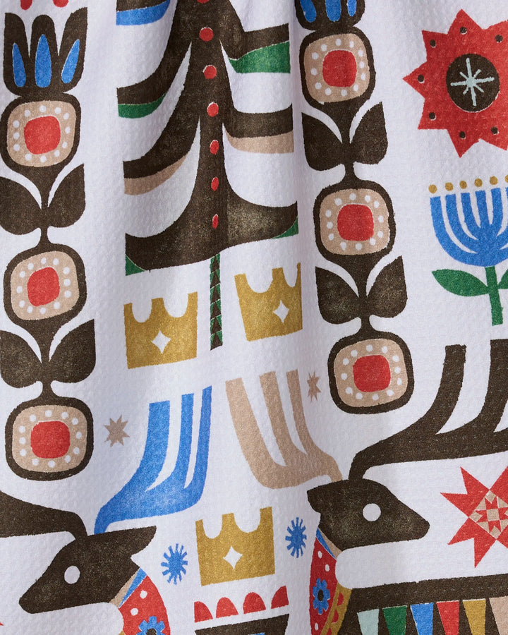 The Everfolk kitchen towel by Geometry features a vibrant folk art pattern with reindeer, flowers, trees, crowns, and geometric shapes in bold colors on white—eco-friendly and perfect for adding charm to your kitchen.