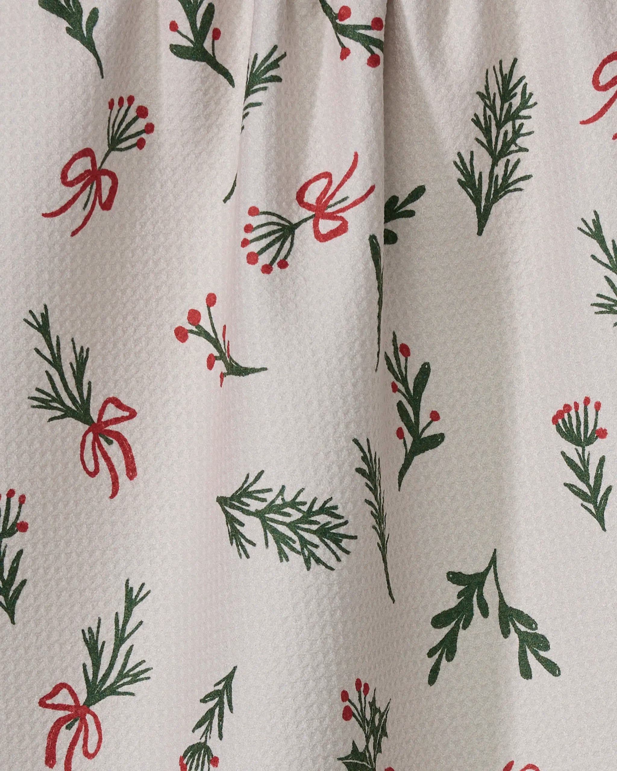 The Geometry Everlove tea towel features a white textured fabric adorned with green leafy branches, red bows, and berries—a festive holiday design perfect for brightening up your kitchen.