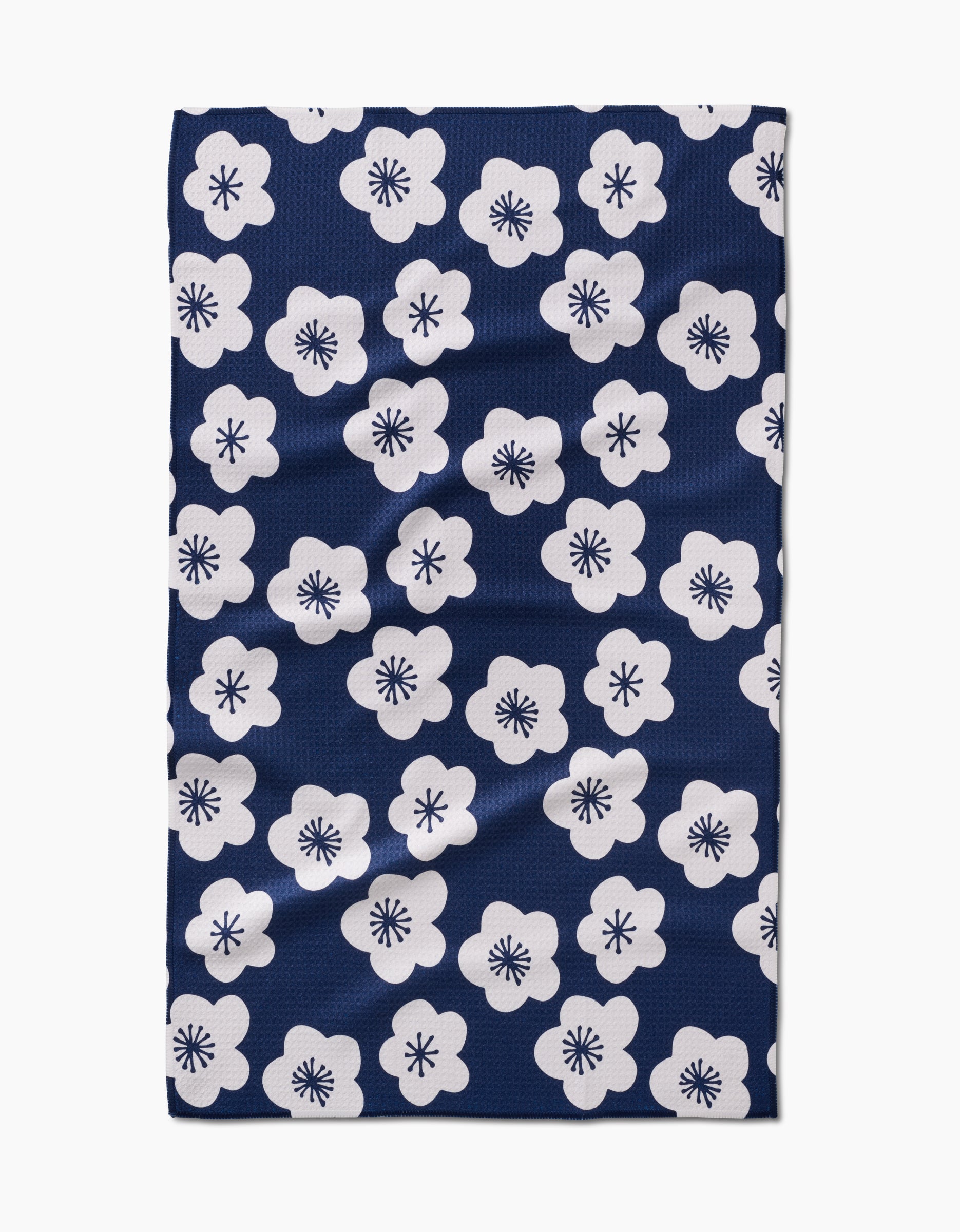 The GEOMETRY Every Sunday tea towel is dark blue, made from recycled materials, and features an even pattern of white five-petal flowers with black starburst centers.