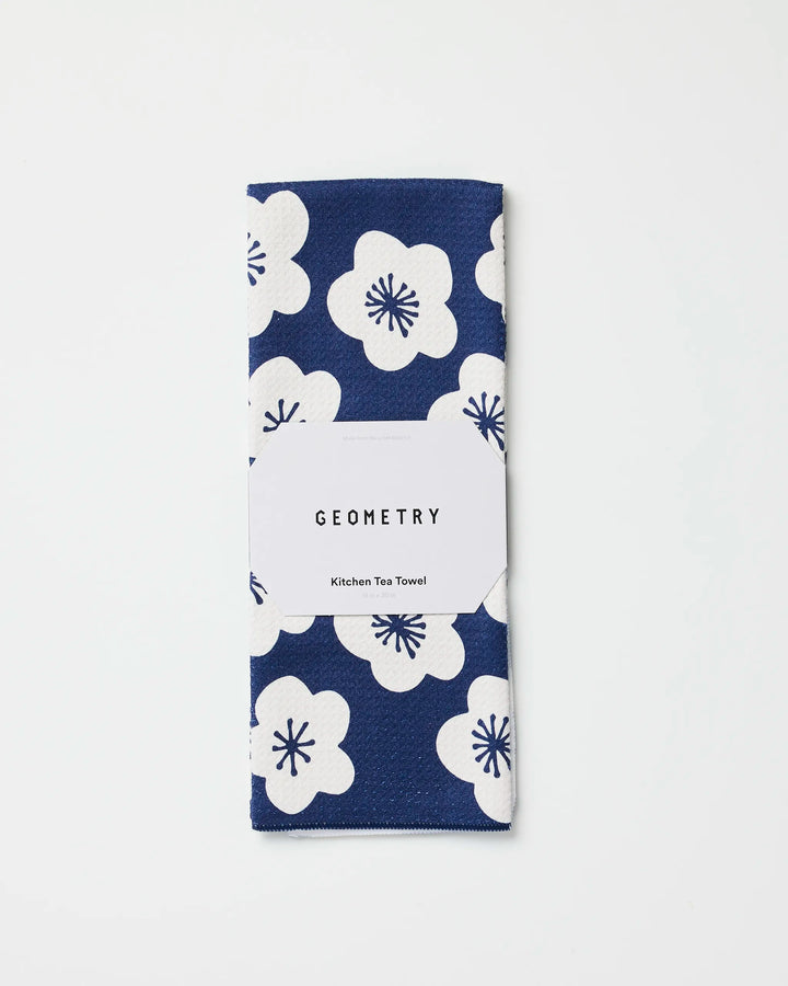 A folded blue tea towel with a white floral pattern, made from recycled materials and labeled "GEOMETRY Every Sunday," is displayed on a plain white background.