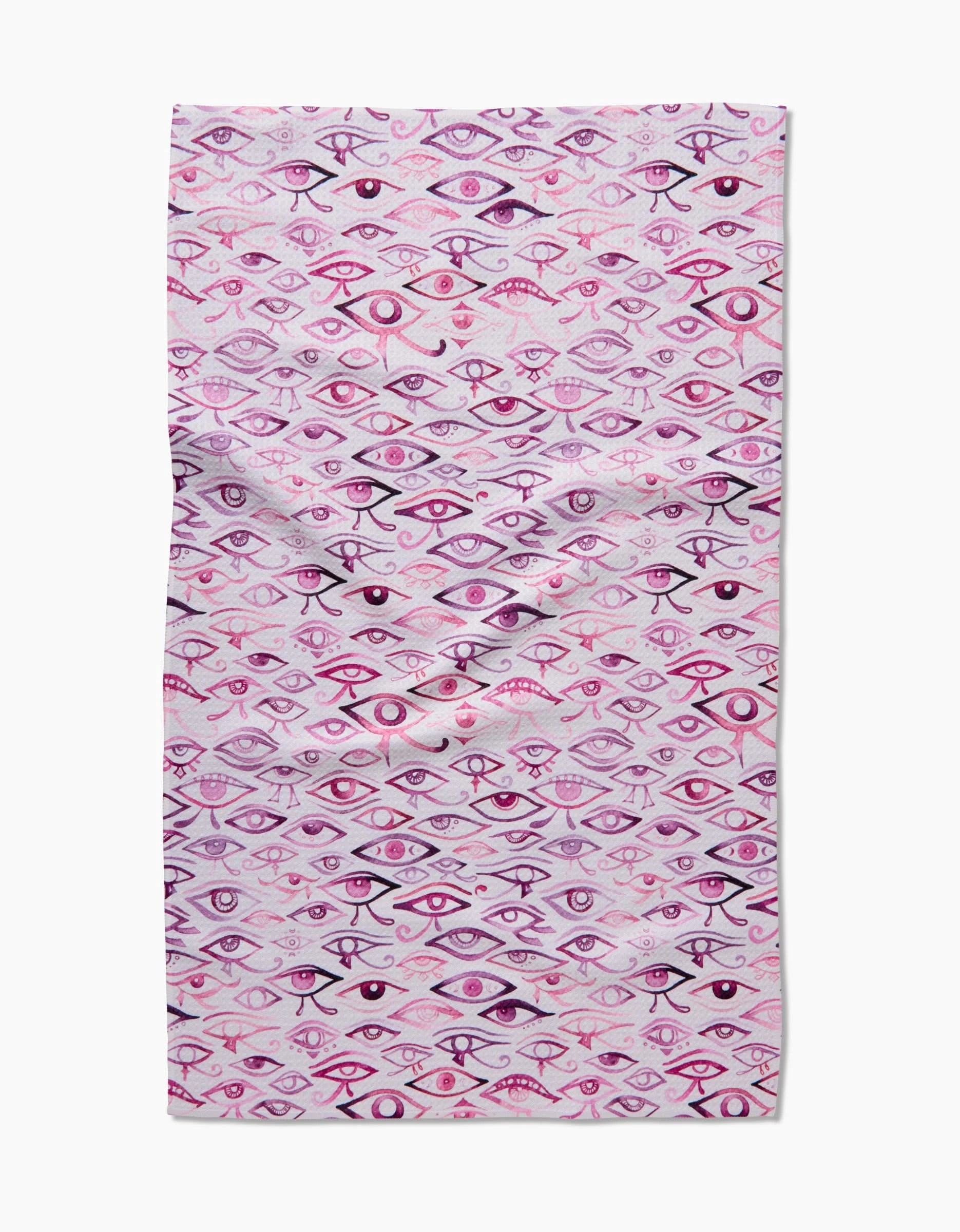 The Eye Of Horus tea towel by Maayan Alper-Swan features a hand-drawn eyes pattern in pink, purple, and black on light pink Geoweave fabric—slightly wrinkled for unique kitchen style.