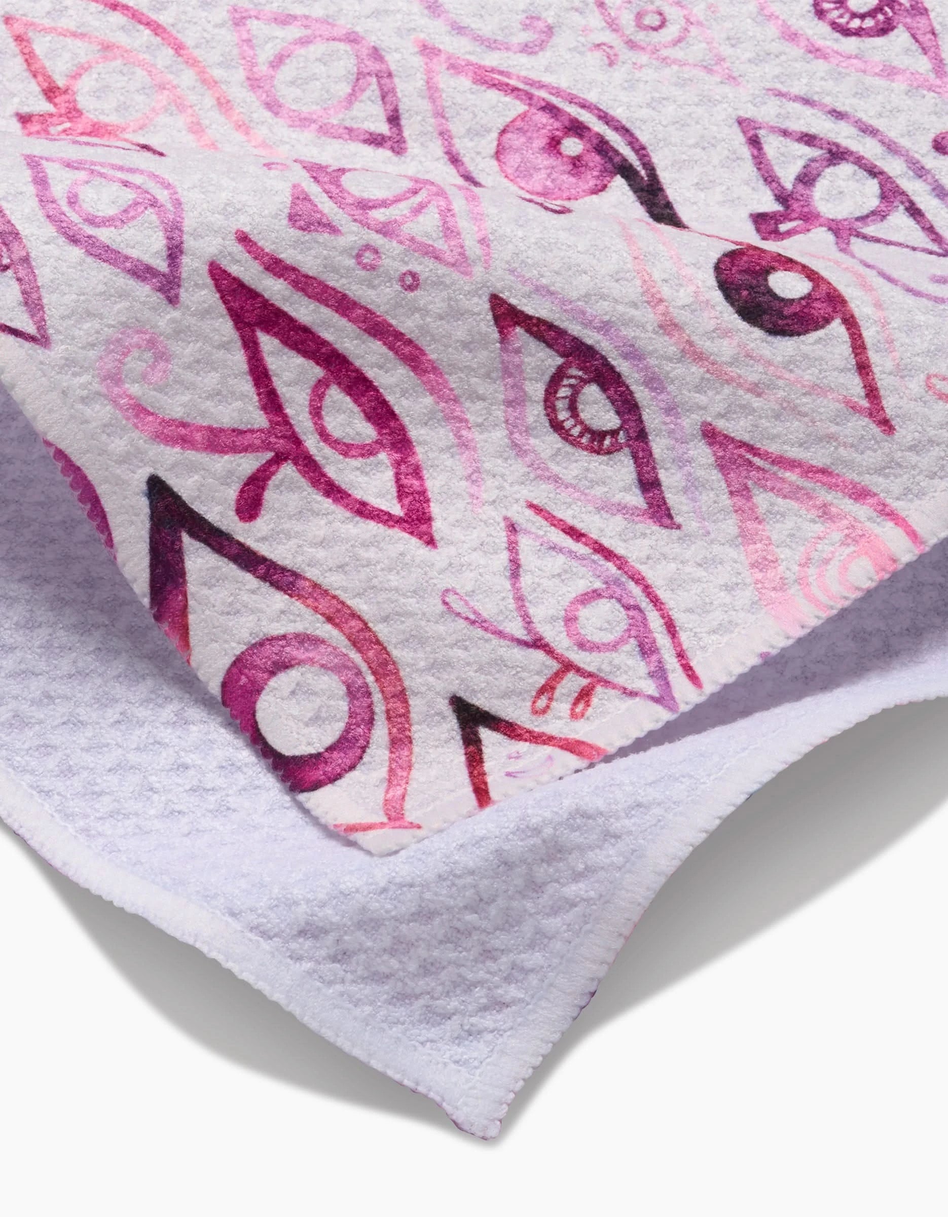 A close-up of the Maayan Alper-Swan Eye Of Horus tea towel, folded to display its Geoweave white fabric with a vibrant pink and purple abstract eye pattern on the front and a textured plain underside.