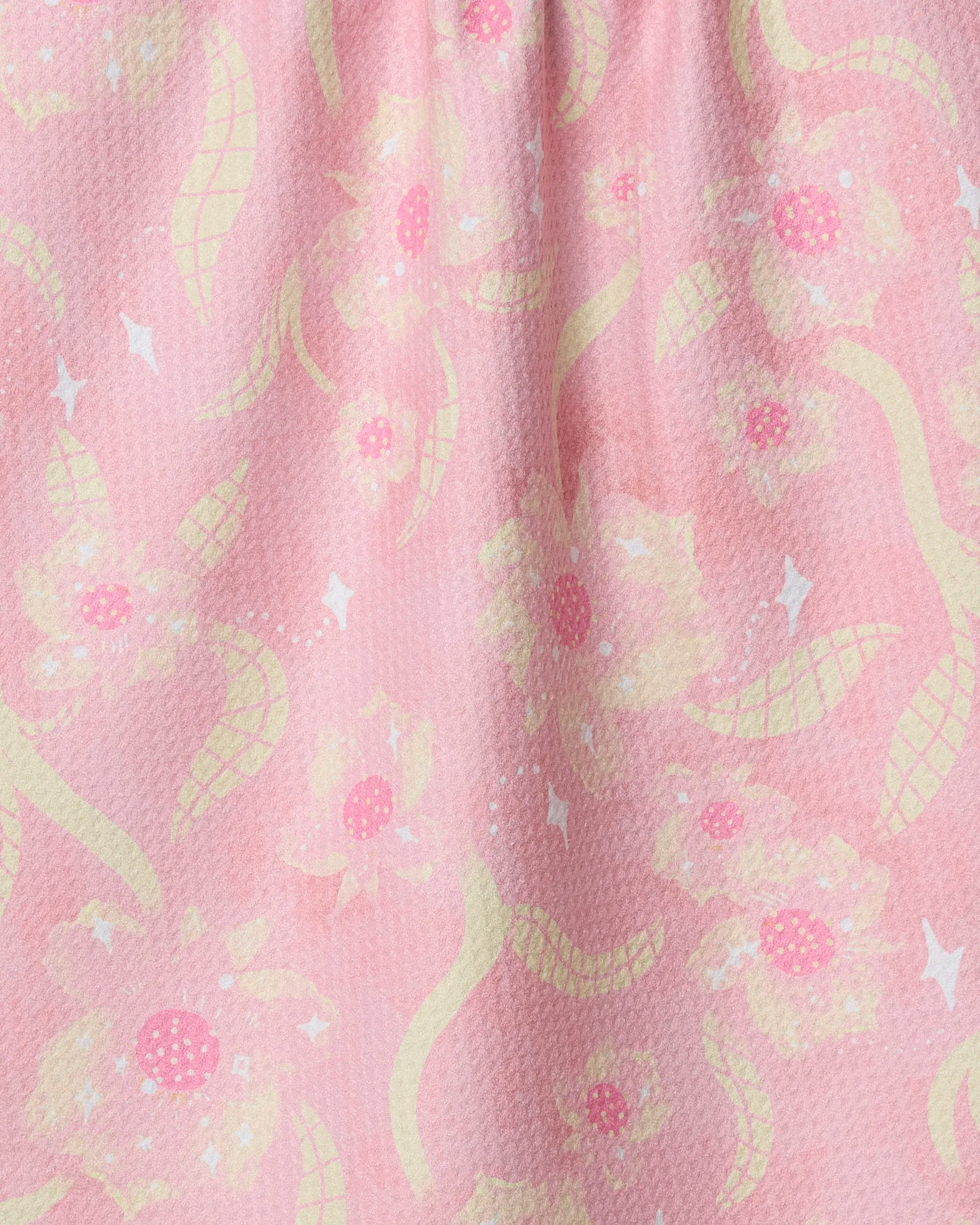 The Fairy Dust Floral tea towel by Geometry features soft pink fabric with yellow and white abstract flowers, curving shapes, and white diamond accents—ultra-absorbent for kitchen use.