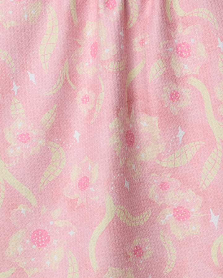 The Fairy Dust Floral tea towel by Geometry features soft pink fabric with yellow and white abstract flowers, curving shapes, and white diamond accents—ultra-absorbent for kitchen use.