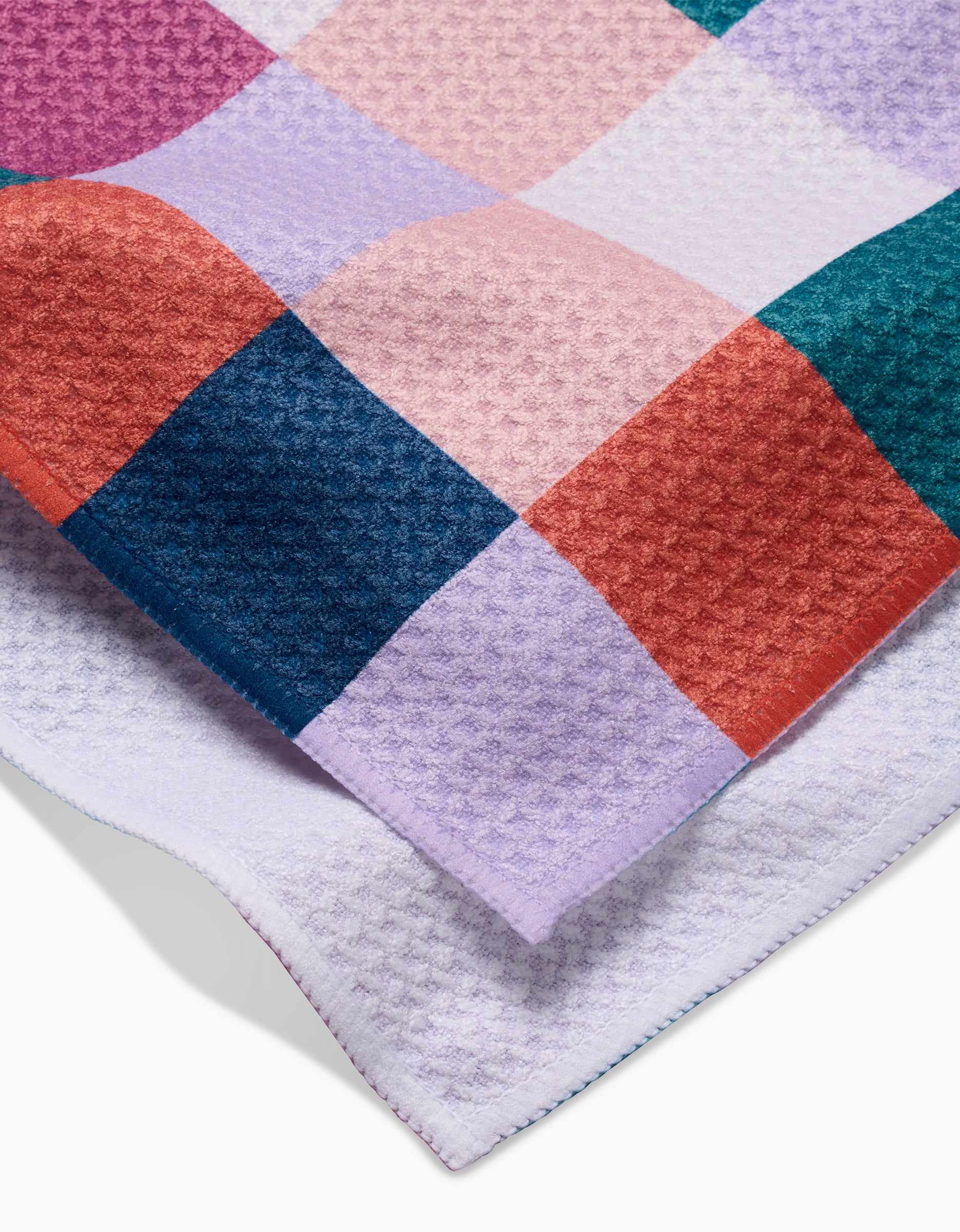 A close-up of Claire Iglesias’ Fall Checkers tea towel, crafted from soft Geoweave fabric and featuring a colorful checkerboard pattern in shades of purple, pink, red, blue, and green with a waffle-like texture.