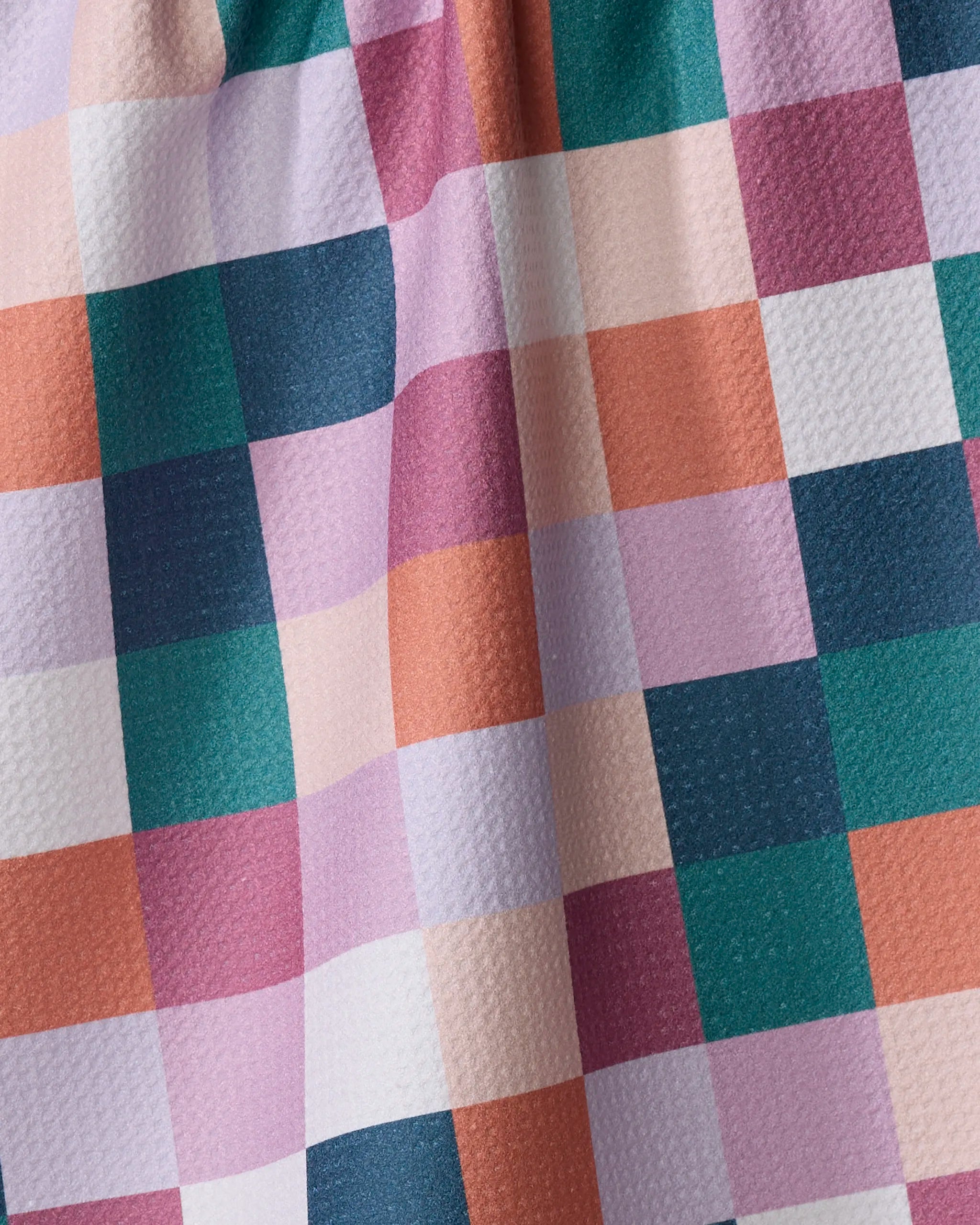 A close-up of Fall Checkers by Claire Iglesias—a vibrant kitchen towel with a pink, orange, teal, white, and purple checkered pattern. Slightly gathered at the top and made from recycled materials.