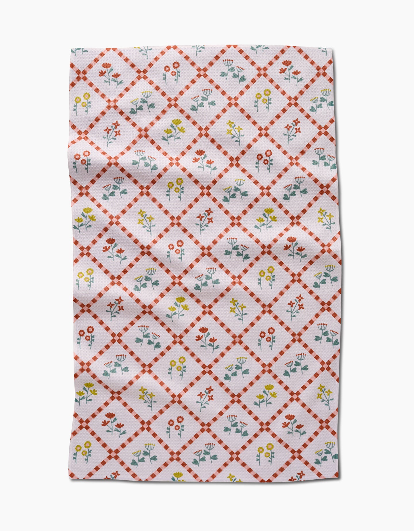 The Fall Flowers tea towel by Claire Iglesias is white with a red diamond lattice and vibrant yellow, red, and blue floral designs inside each diamond. This ultra-absorbent kitchen towel features some visible folds and wrinkles.