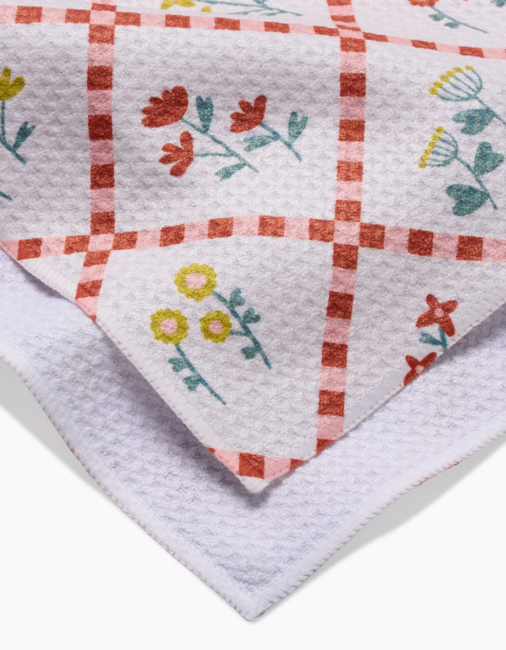 A close-up of Claire Iglesias Fall Flowers kitchen towel, ultra-absorbent with a red checkered pattern and colorful yellow, red, and blue floral designs. The folded tea towel shows both printed and plain white textured sections.