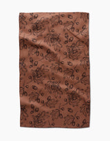 The Fall Foliage kitchen towel by Aubrey Fairchild features eco-friendly brown fabric with a black oak leaf and acorn pattern, creating an autumnal, botanical vibe. Laid flat with slight wrinkles, it makes a charming addition to any kitchen.