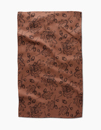 The Fall Foliage kitchen towel by Aubrey Fairchild features eco-friendly brown fabric with a black oak leaf and acorn pattern, creating an autumnal, botanical vibe. Laid flat with slight wrinkles, it makes a charming addition to any kitchen.