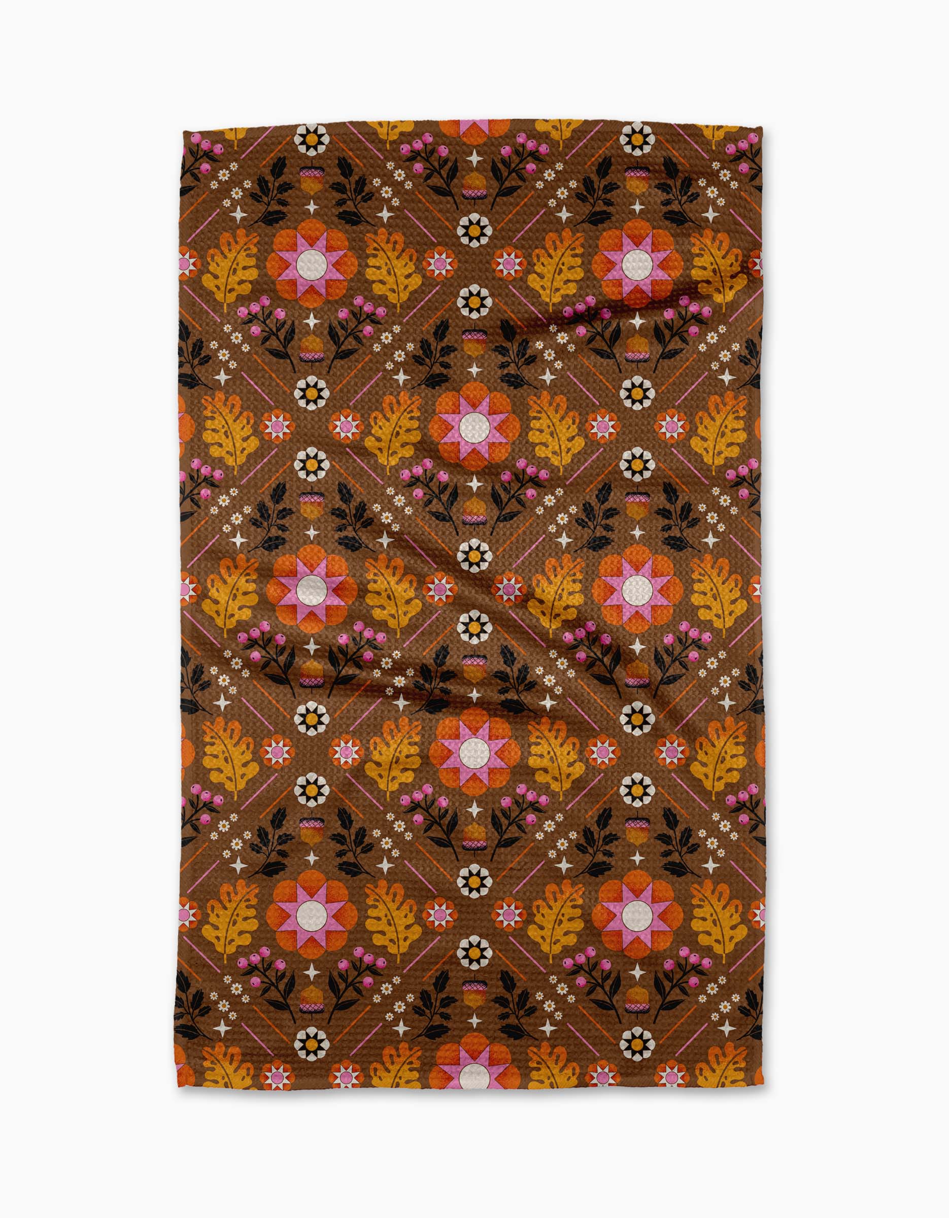 The Fall Folk tea towel by Megan Roy is brown, made from recycled materials, and features a symmetrical geometric floral pattern in pink, orange, yellow, black, and white with repeating flowers, leaves, and dots.