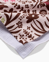 A close-up of the Kayla Ann Fall Fowl Tea Towel features a brown floral pattern on pale pink, with the corner flipped to reveal its white recycled underside.