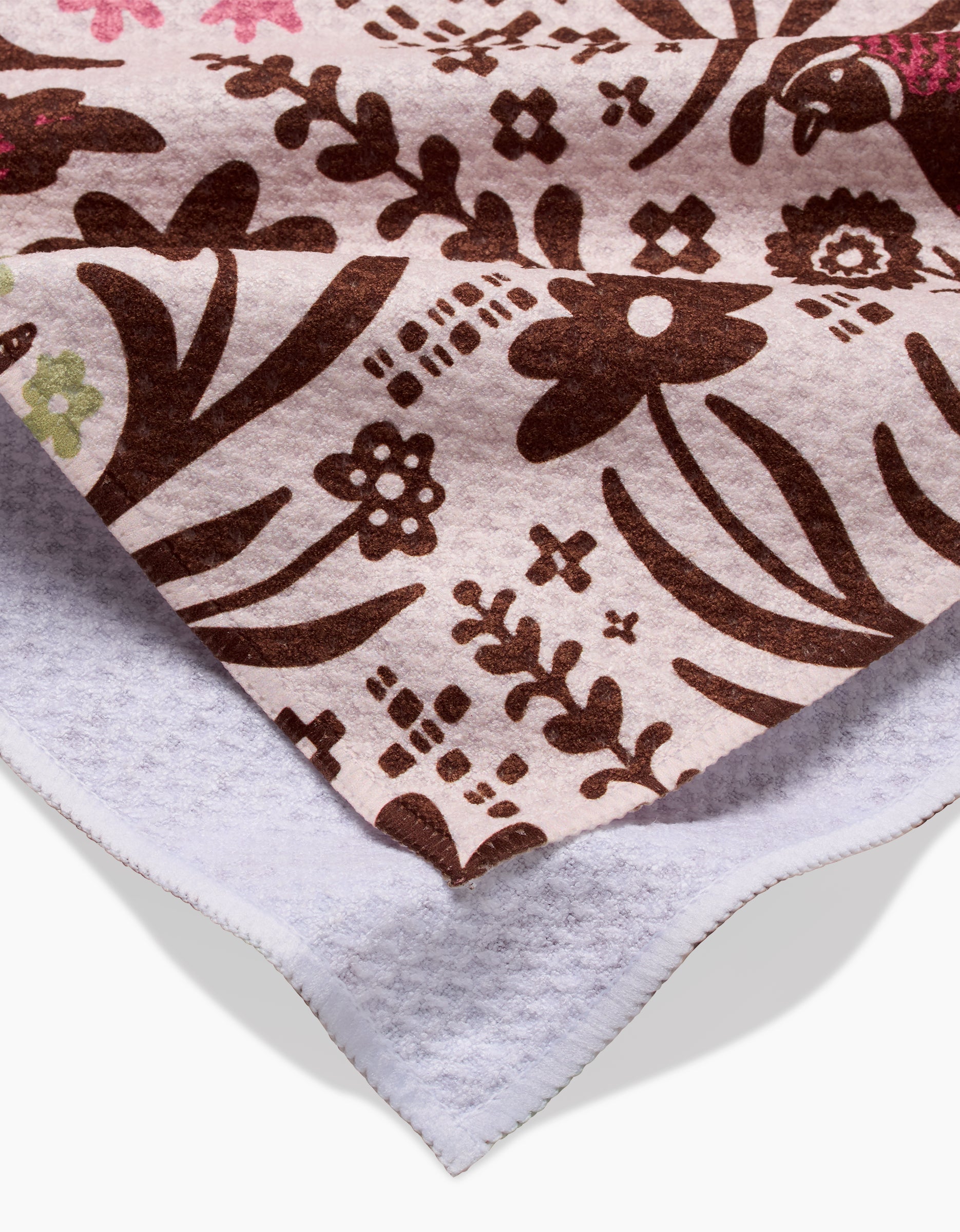 A close-up of the Kayla Ann Fall Fowl Tea Towel features a brown floral pattern on pale pink, with the corner flipped to reveal its white recycled underside.